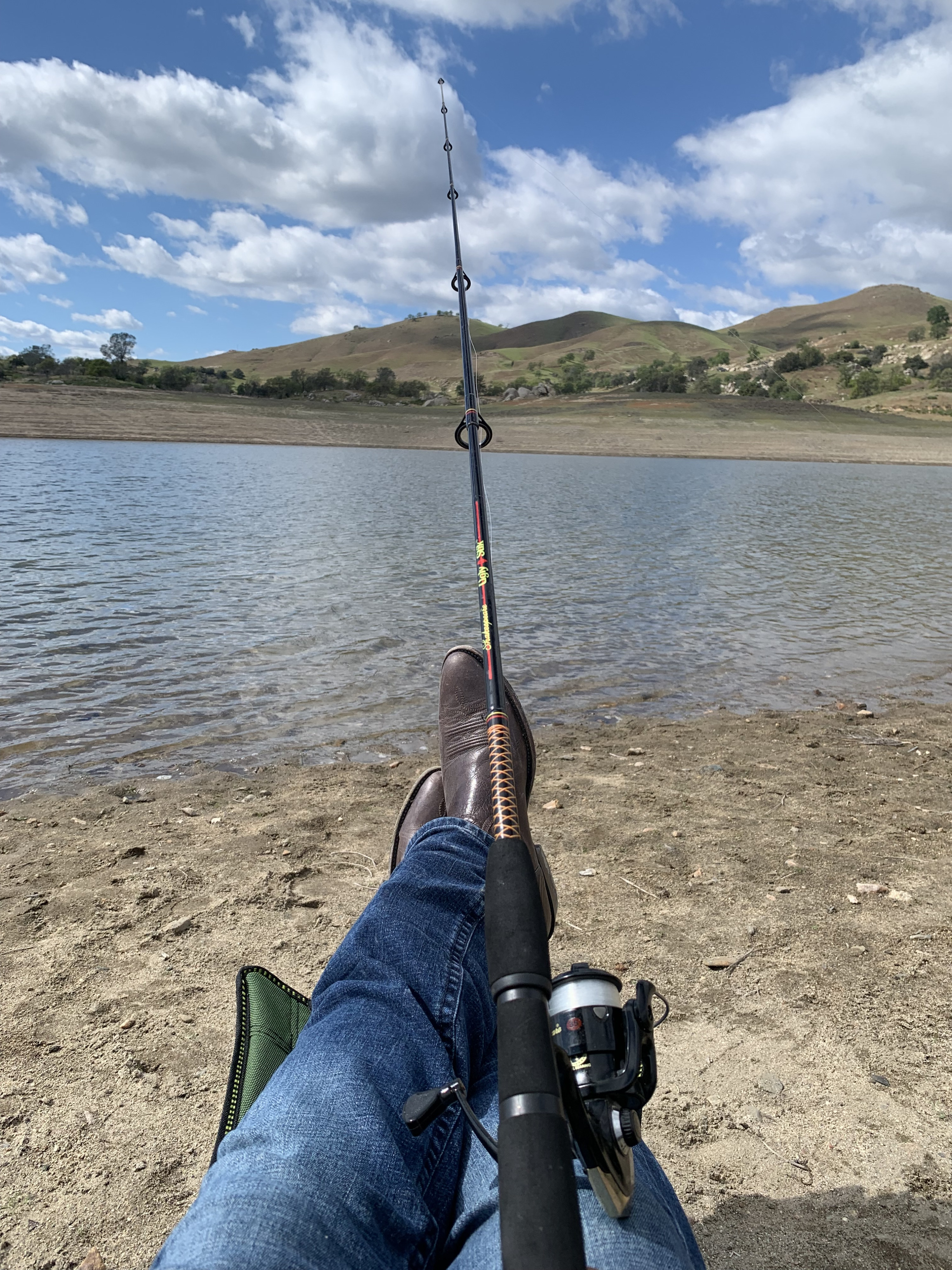 Person in jeans and boots fishing by a scenic lake under a cloudy sky. A perfect, relaxing outdoor stop for an RV rental trip.. Thor Scope 2022