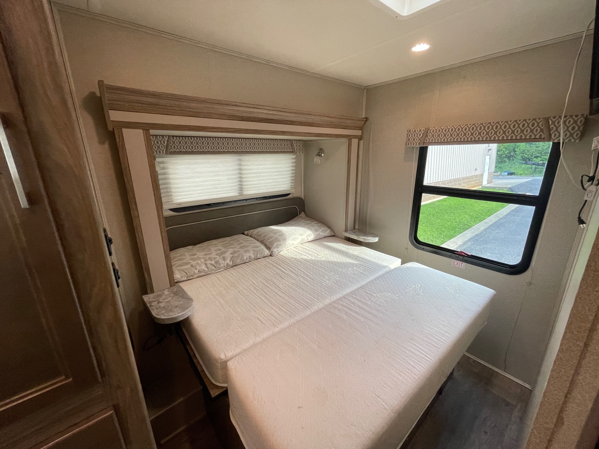 An RV rental bedroom showcasing a large, light-colored bed, small side tables, and a window with an outdoor view.. Entegra Coach Odyssey 2018