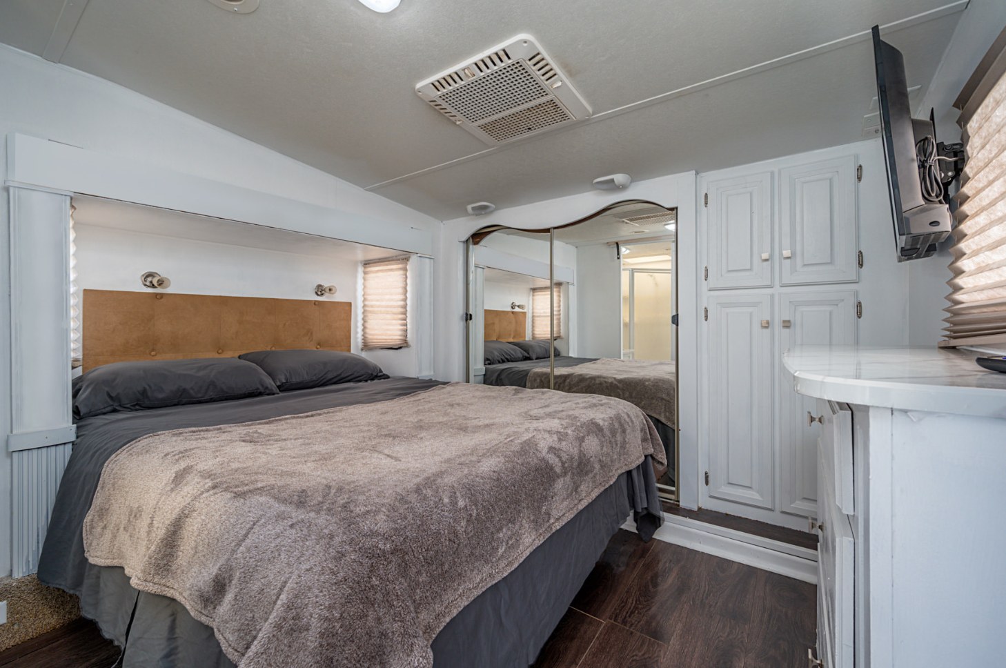 RV rental bedroom with a comfy bed, mirrored closet, wall-mounted TV, and dark wood floors.. Jayco Eagle 2012
