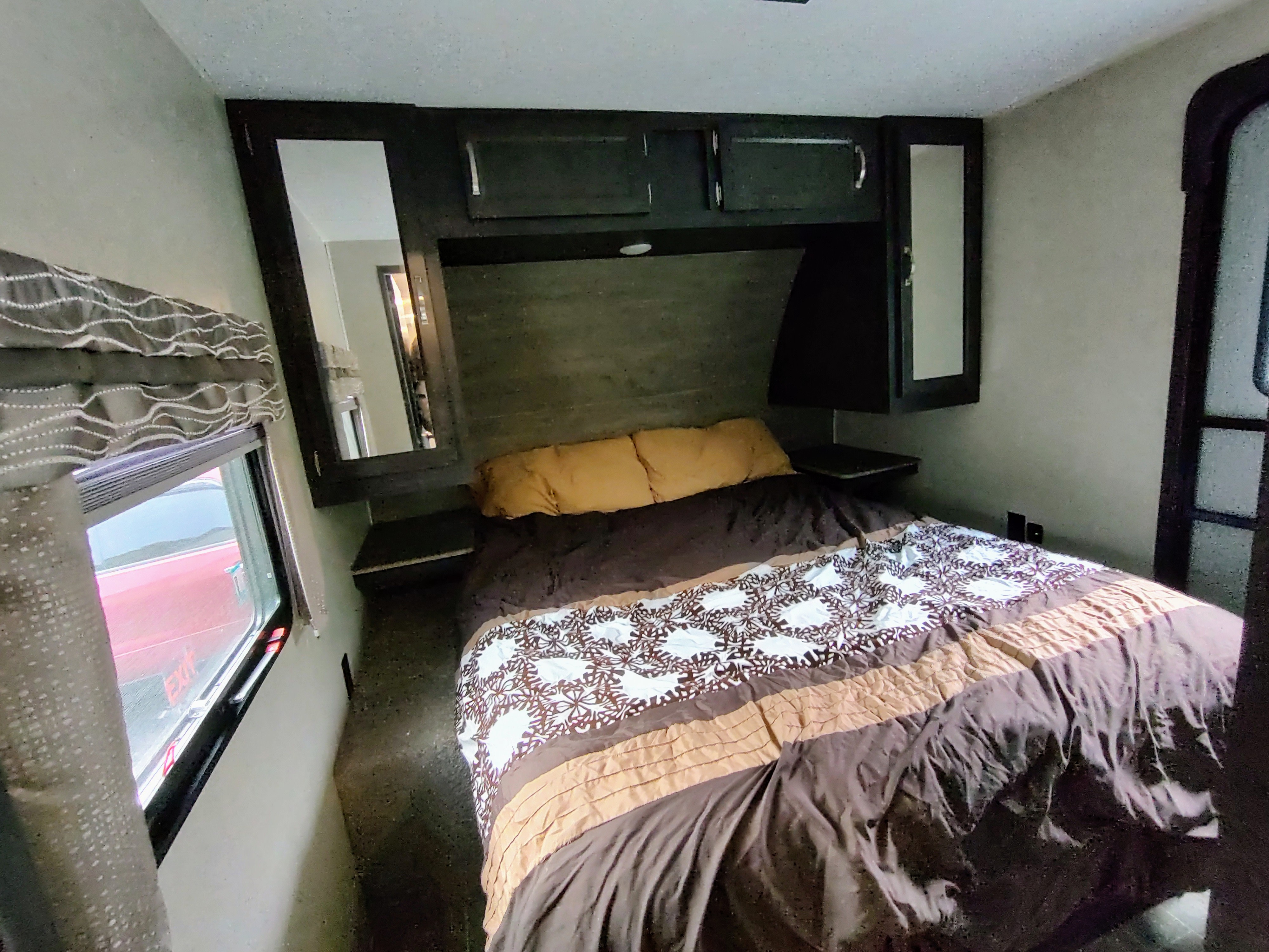 Cozy RV rental bedroom interior with patterned bed, overhead cabinets, and window. Perfect for your next adventure!. Palomino Puma 2020