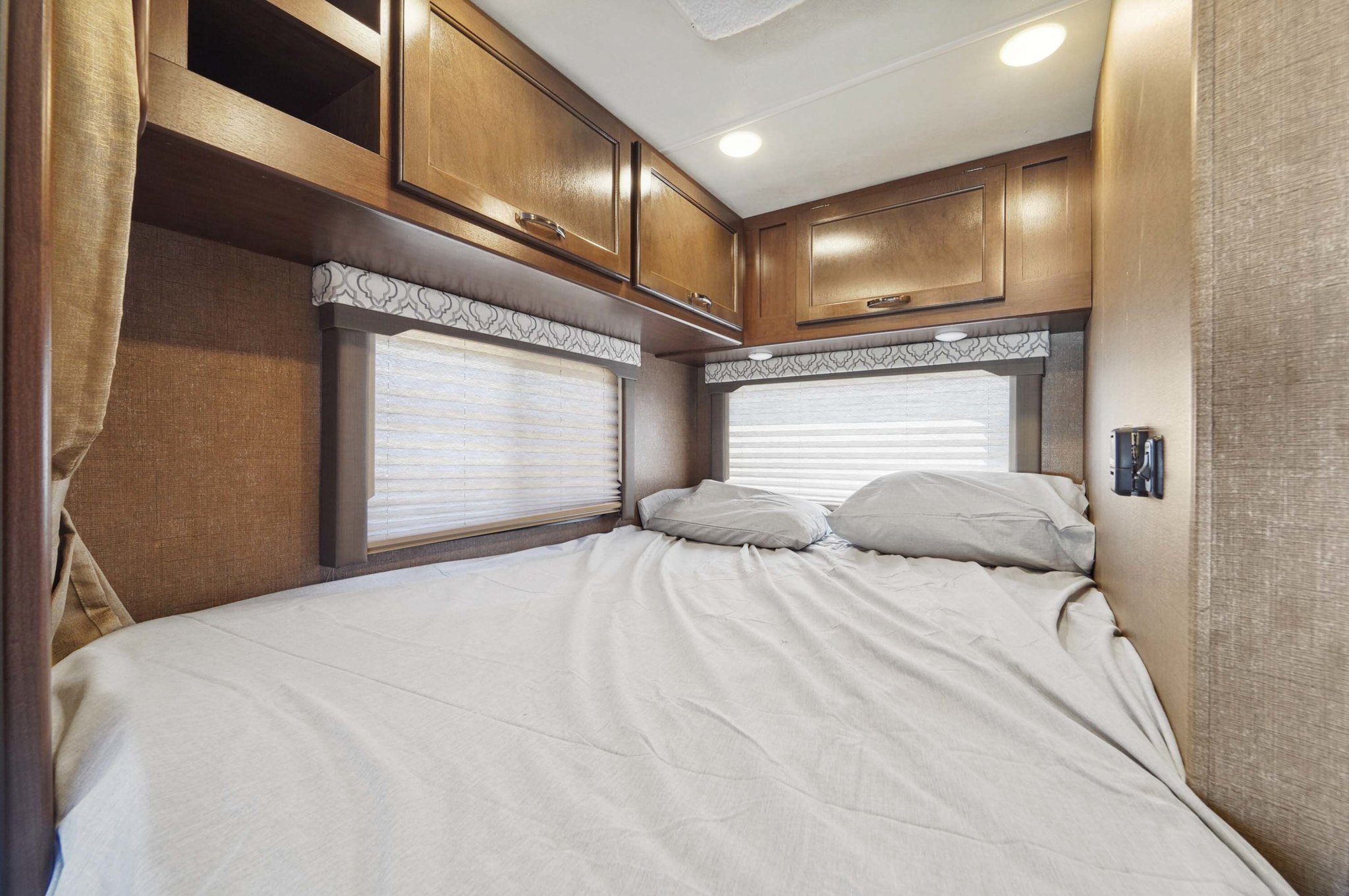 Cozy RV rental bedroom with a comfy bed, overhead cabinets, and window blinds, offering comfort for your travels.. Thor Motor Coach Freedom Elite 2019