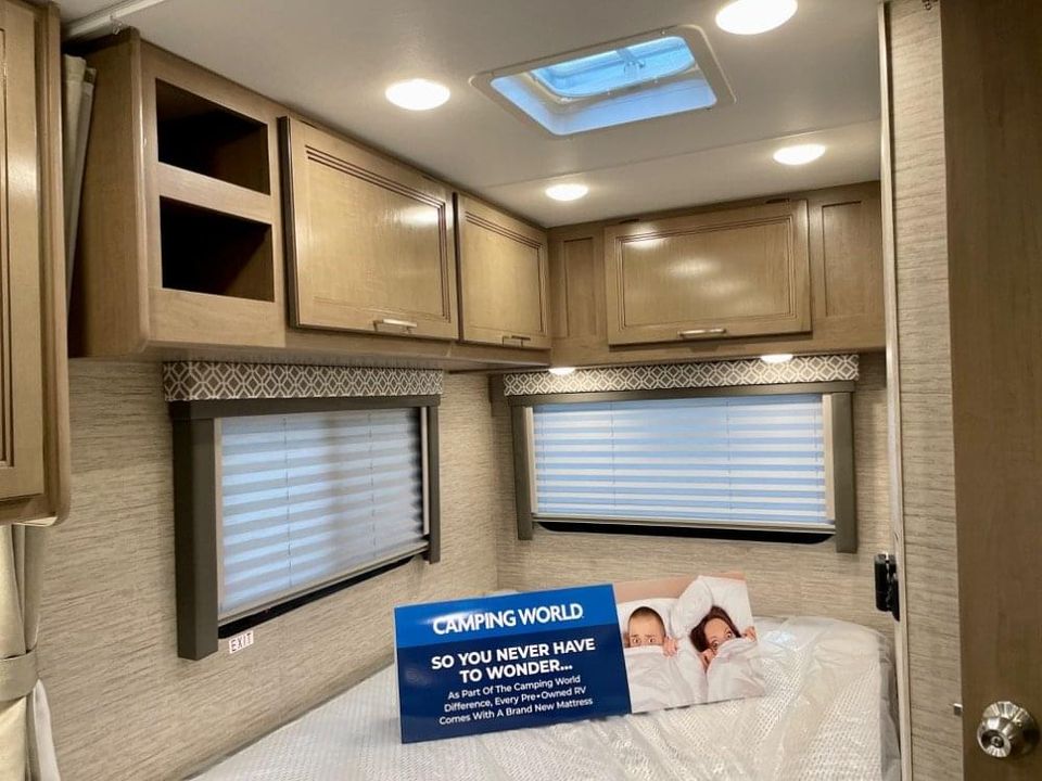 Spacious RV rental bedroom with wood cabinets, two windows, and a bed. A ceiling skylight brightens the space.. Thor Coleman 2022