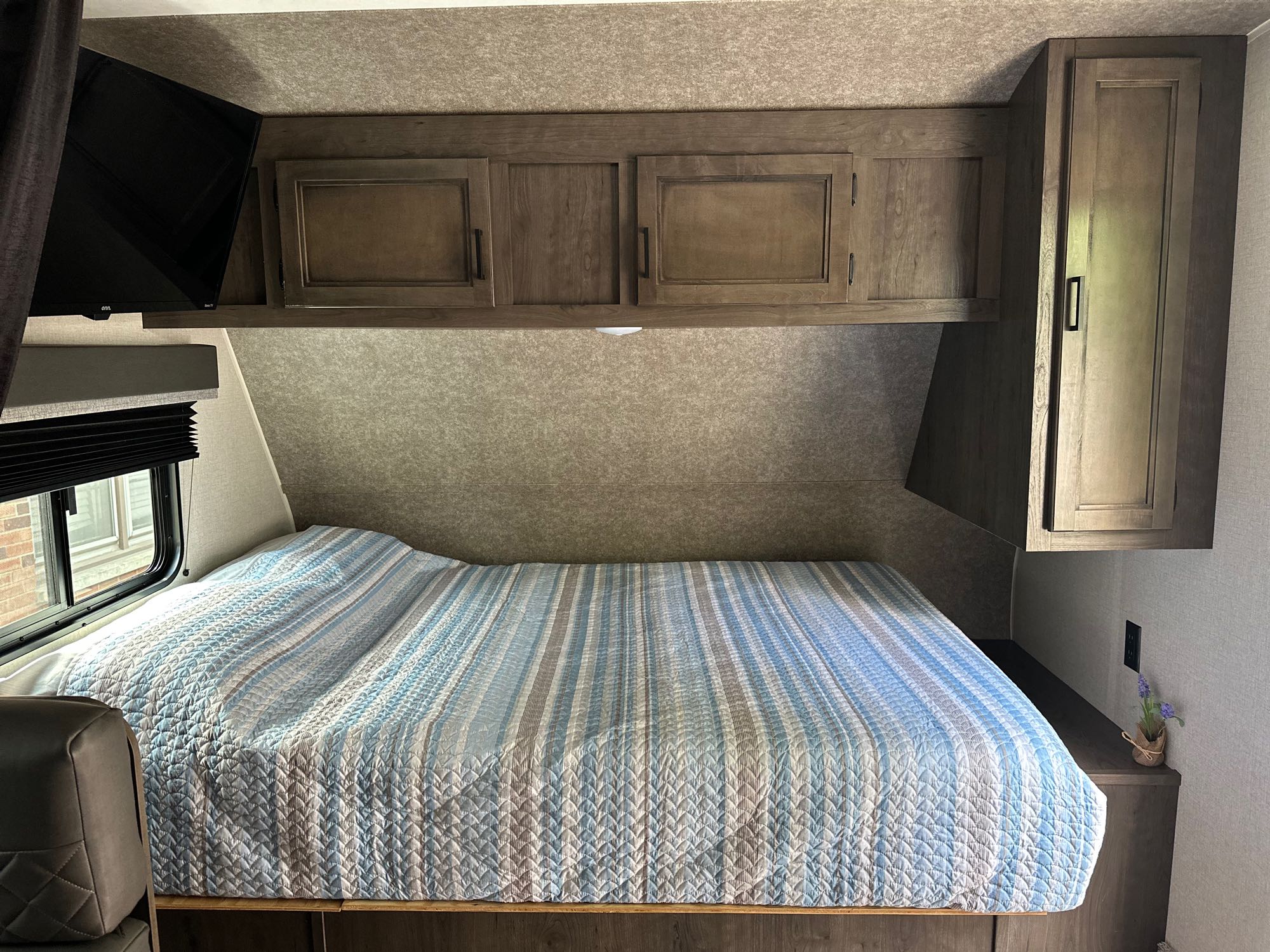RV rental bedroom with striped bed, wooden overhead cabinets, and TV. A comfortable and functional space.. Starcraft Autumn Ridge Mini 180 2021