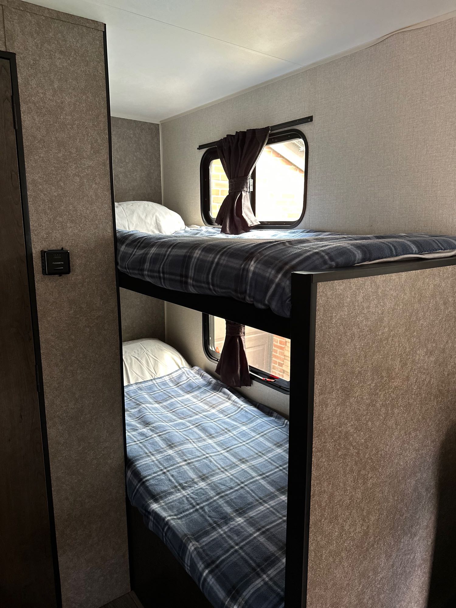 This RV rental features stacked bunk beds, each with a pillow and plaid blanket. Ideal for compact sleeping in a travel trailer.. Starcraft Autumn Ridge Mini 180 2021