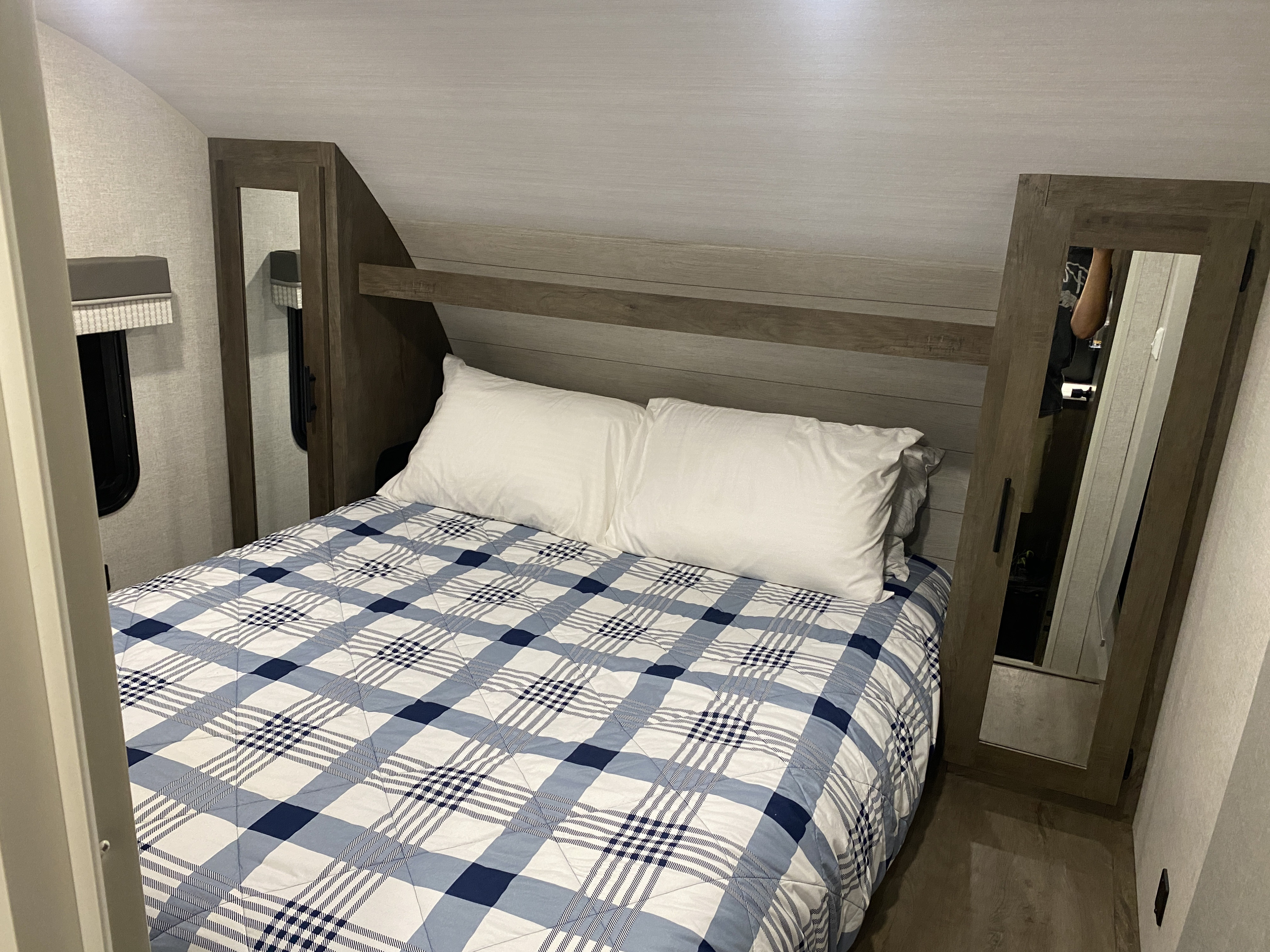 This RV rental features a cozy bedroom with a blue and white plaid bedspread, built-in storage, and mirrors.. Forest River Wildwood X-Lite 2021