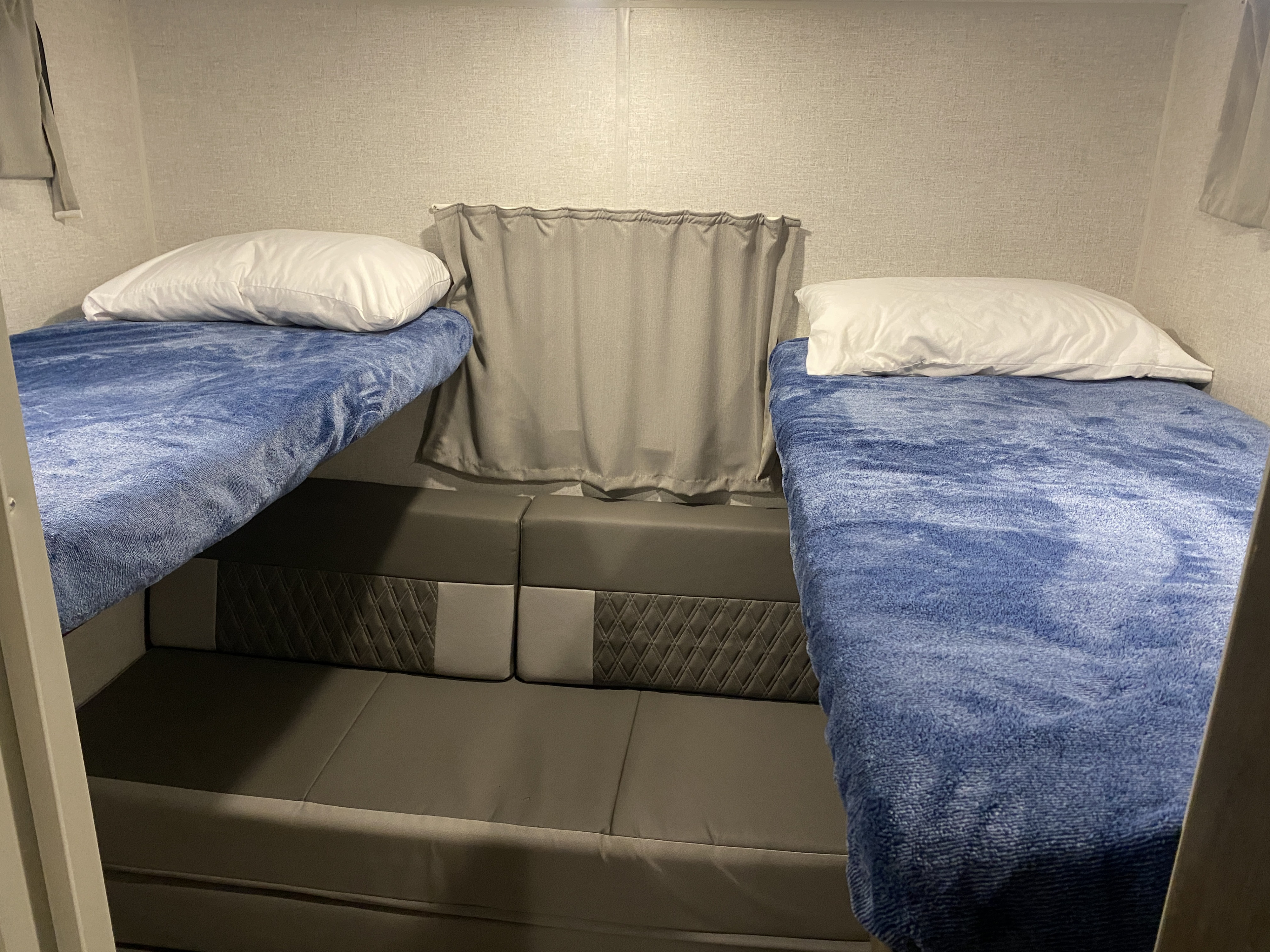 Comfortable rv rental bunk beds with blue blankets and a multi-purpose seating area, ideal for family RV travel.. Forest River Wildwood X-Lite 2021