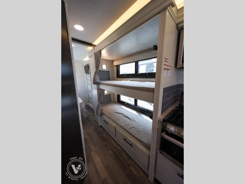 This RV rental interior offers practical bunk beds, a compact kitchen area with a stove, and a view into the rear bathroom.. Jayco Greyhawk 31F 2024
