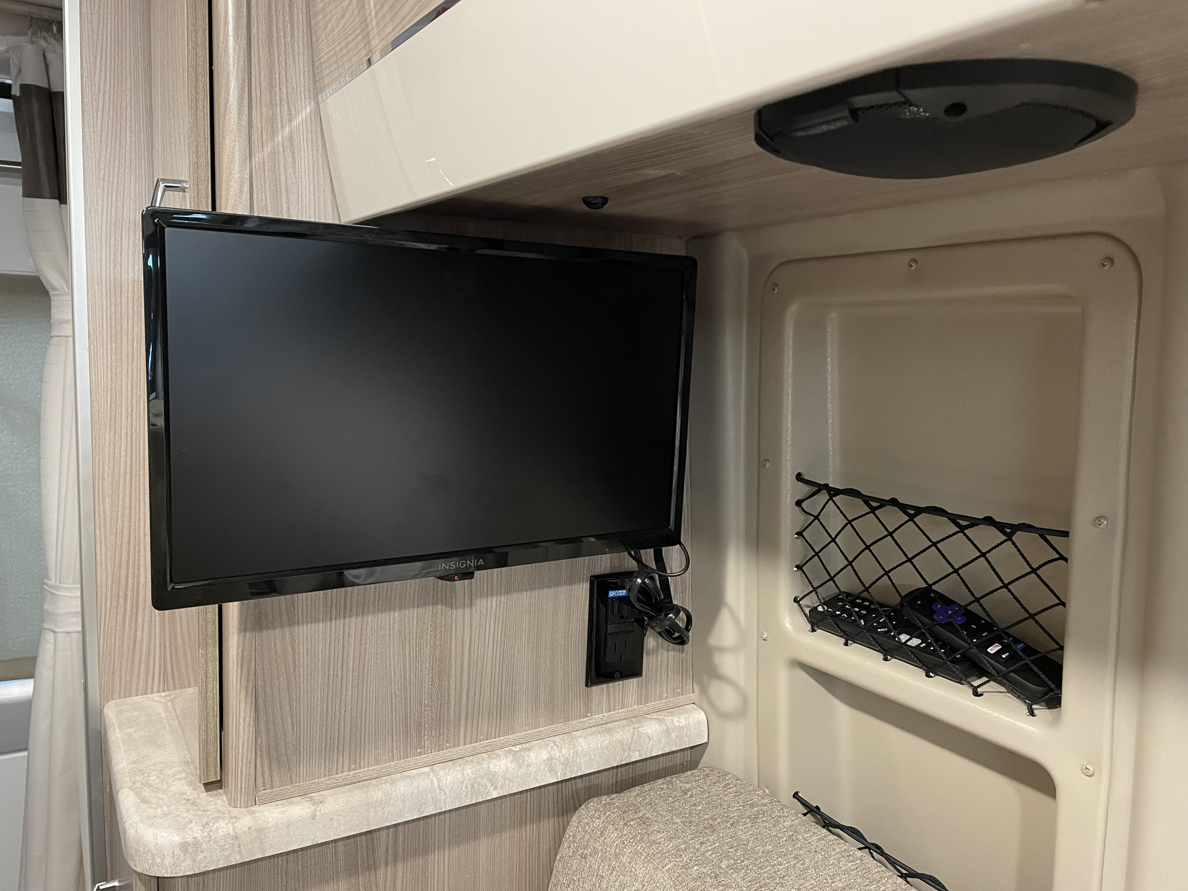 Interior of an RV rental, with an Insignia TV, power outlet, and remotes in a mesh net near seating.. Thor Motor Coach Scope 18M 2023