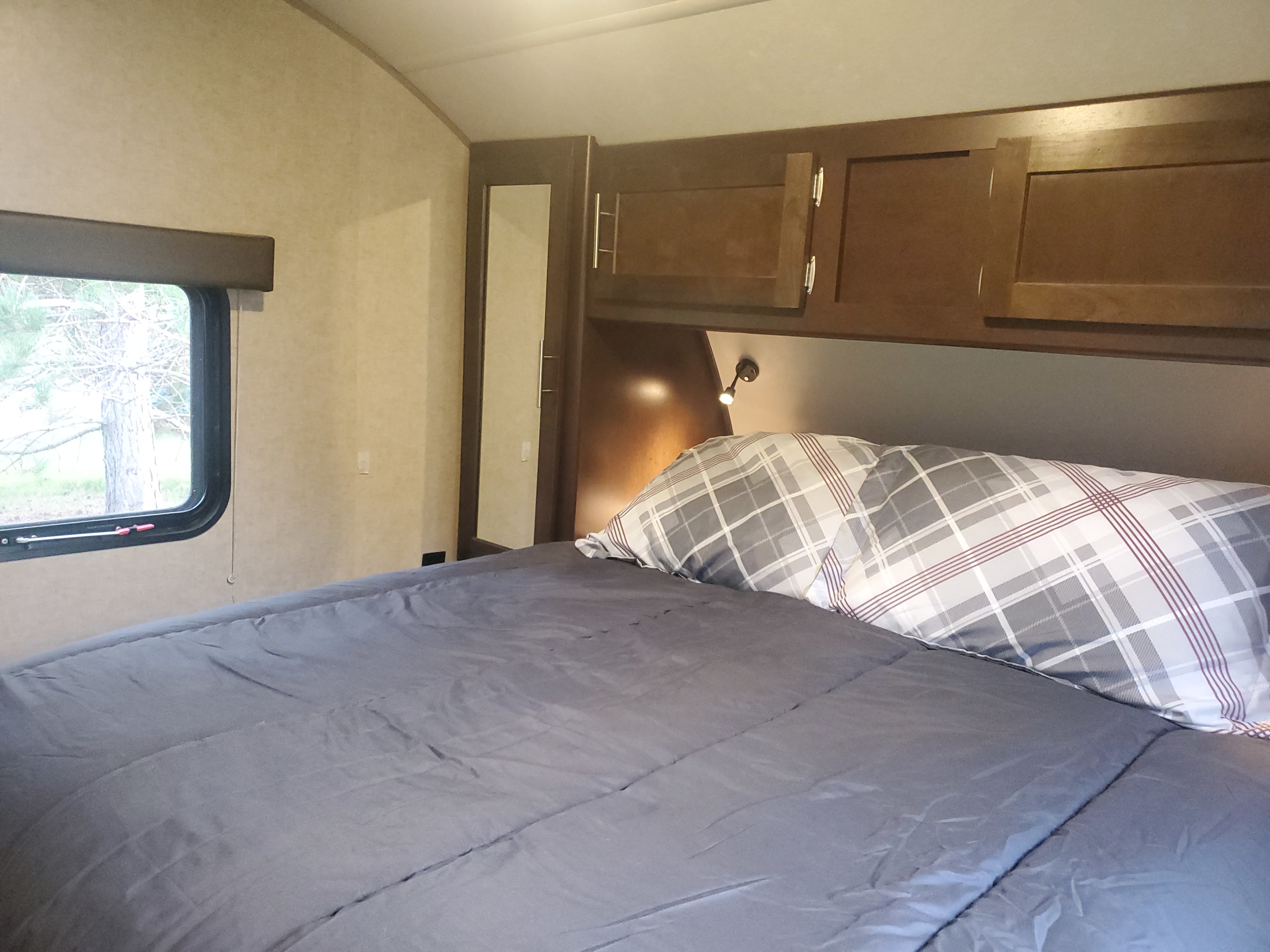 Cozy RV rental bedroom featuring a comfortable bed, plaid pillows, overhead storage, and a window with tree views.. Forest River Cherokee Grey Wolf 2017