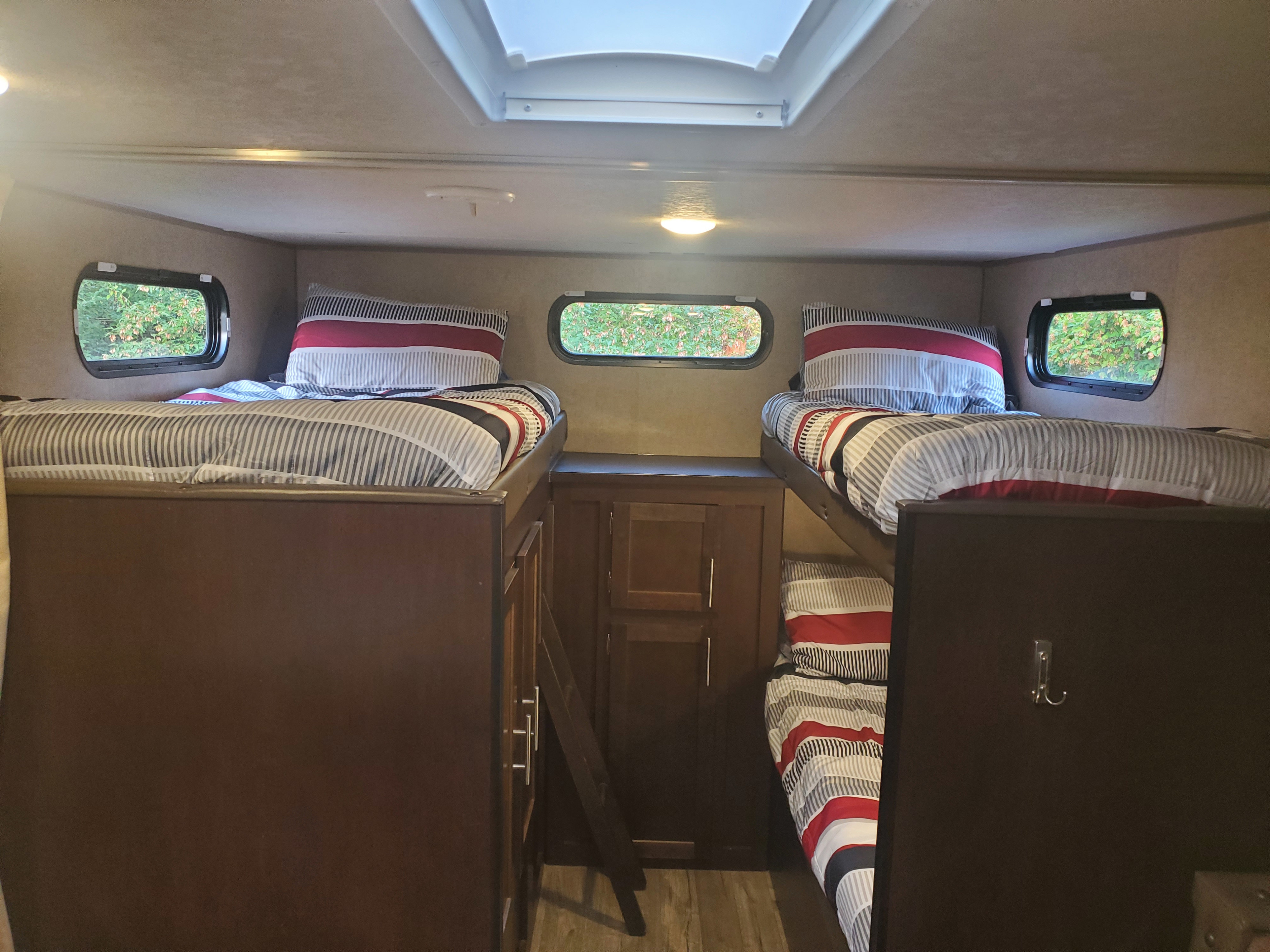 Cozy RV rental interior with four striped bunk beds, a skylight, and windows showing trees. Ideal for family adventures.. Forest River Cherokee Grey Wolf 2017