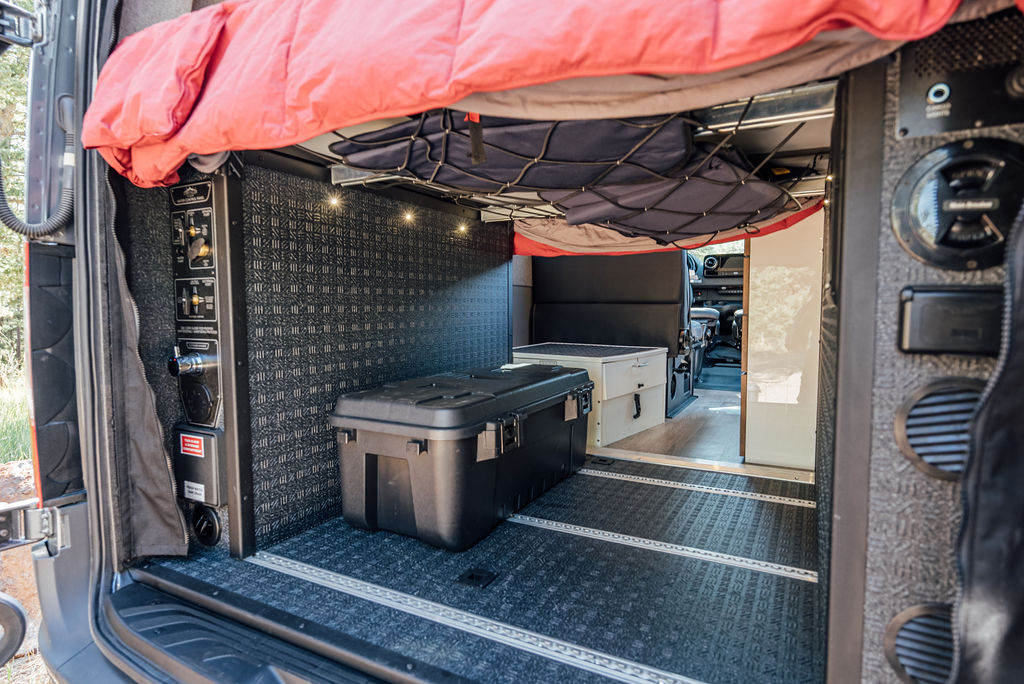 Spacious RV rental interior with overhead bed, storage net, control panel, and large gear box on textured floor.. Storyteller Overland Storyteller Overland Class B 2022