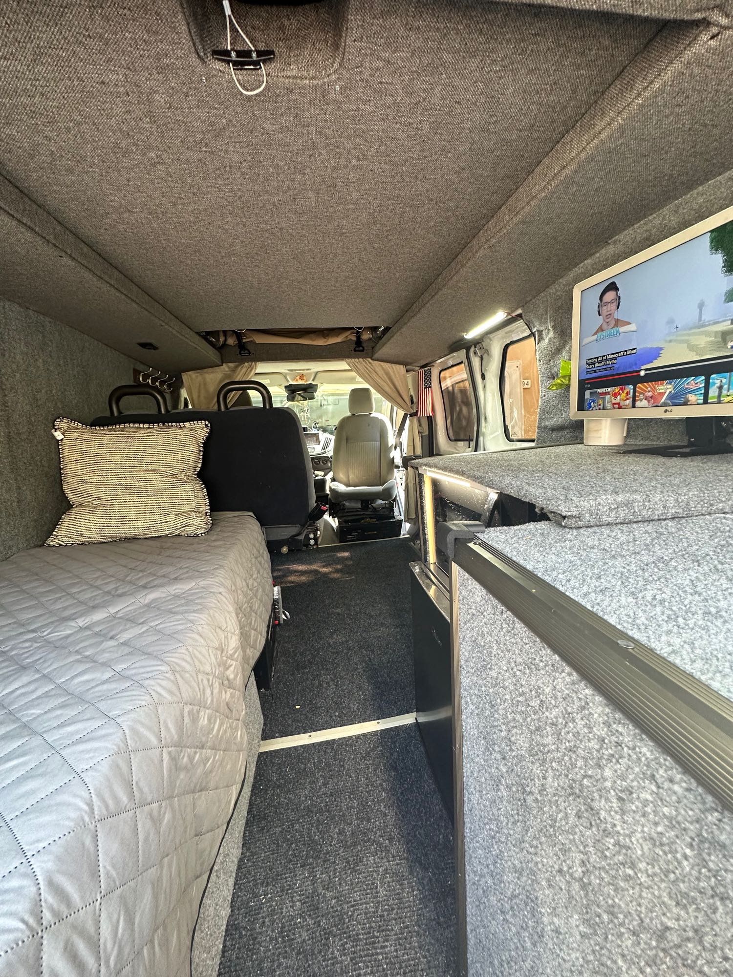 Inside this rv rental, a comfortable van conversion features a bed, entertainment monitor, and carpeted walls.. Ford Transit 2016