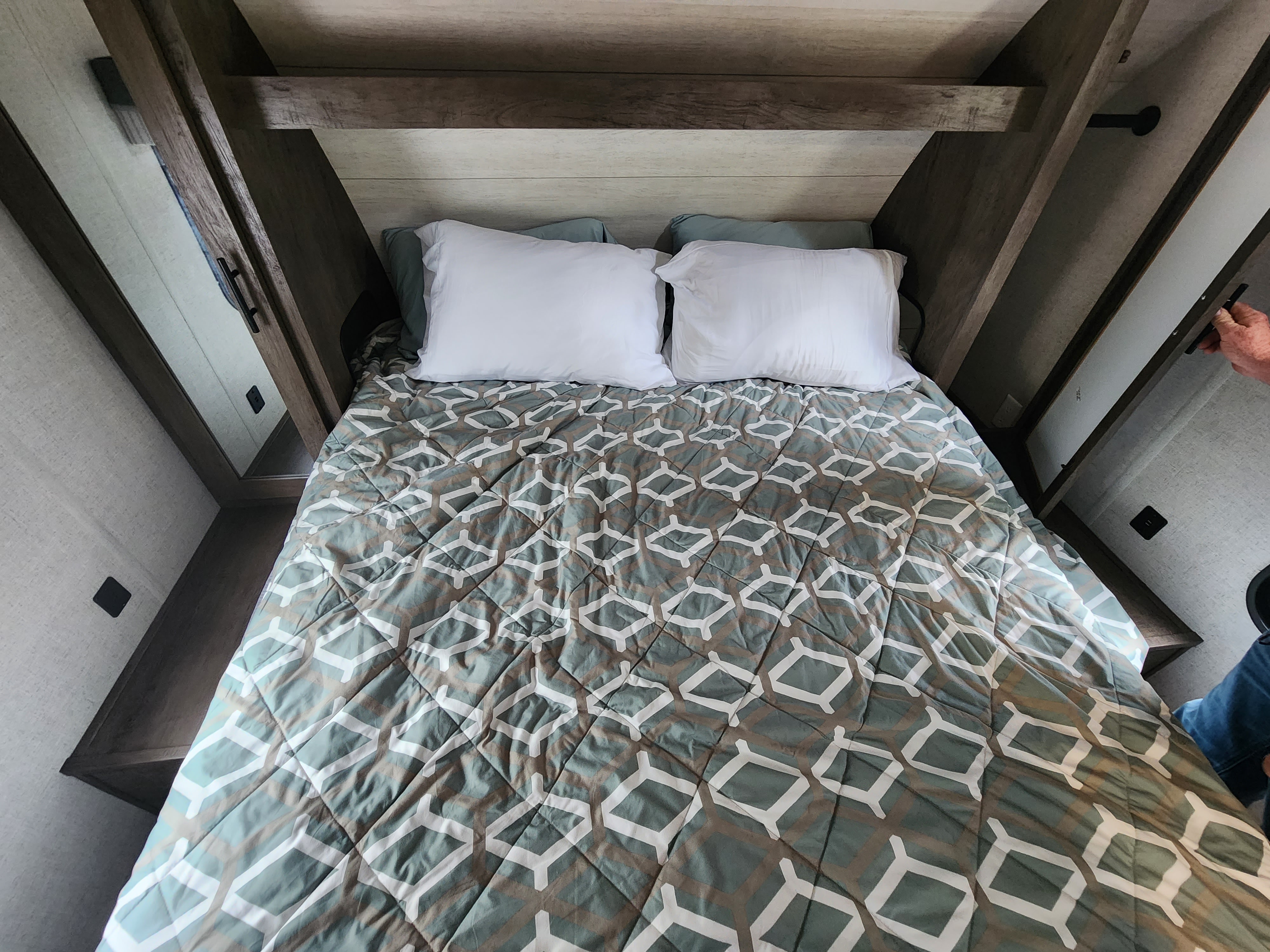 Cozy RV rental bedroom featuring a bed with patterned comforter, white pillows, and built-in storage.. Forest River Wildwood X-Lite 2021