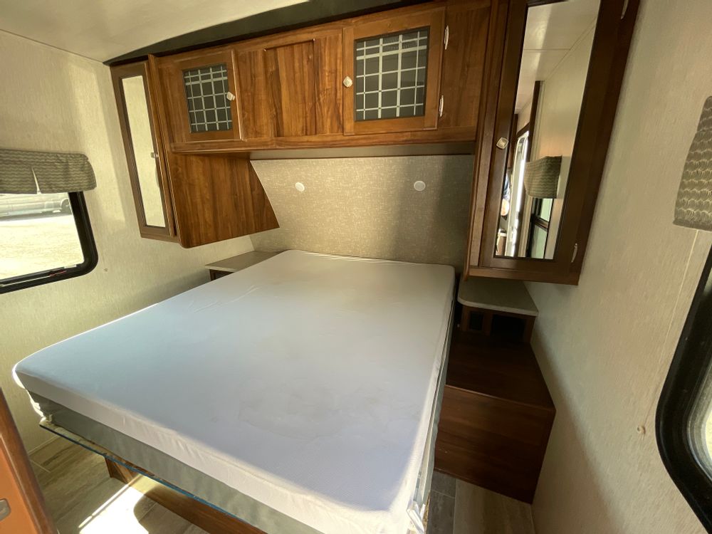 Inside an RV rental: a compact bedroom view with bed, wood overhead cabinets, and mirrored side storage.. Heartland RVs Mallard 2018