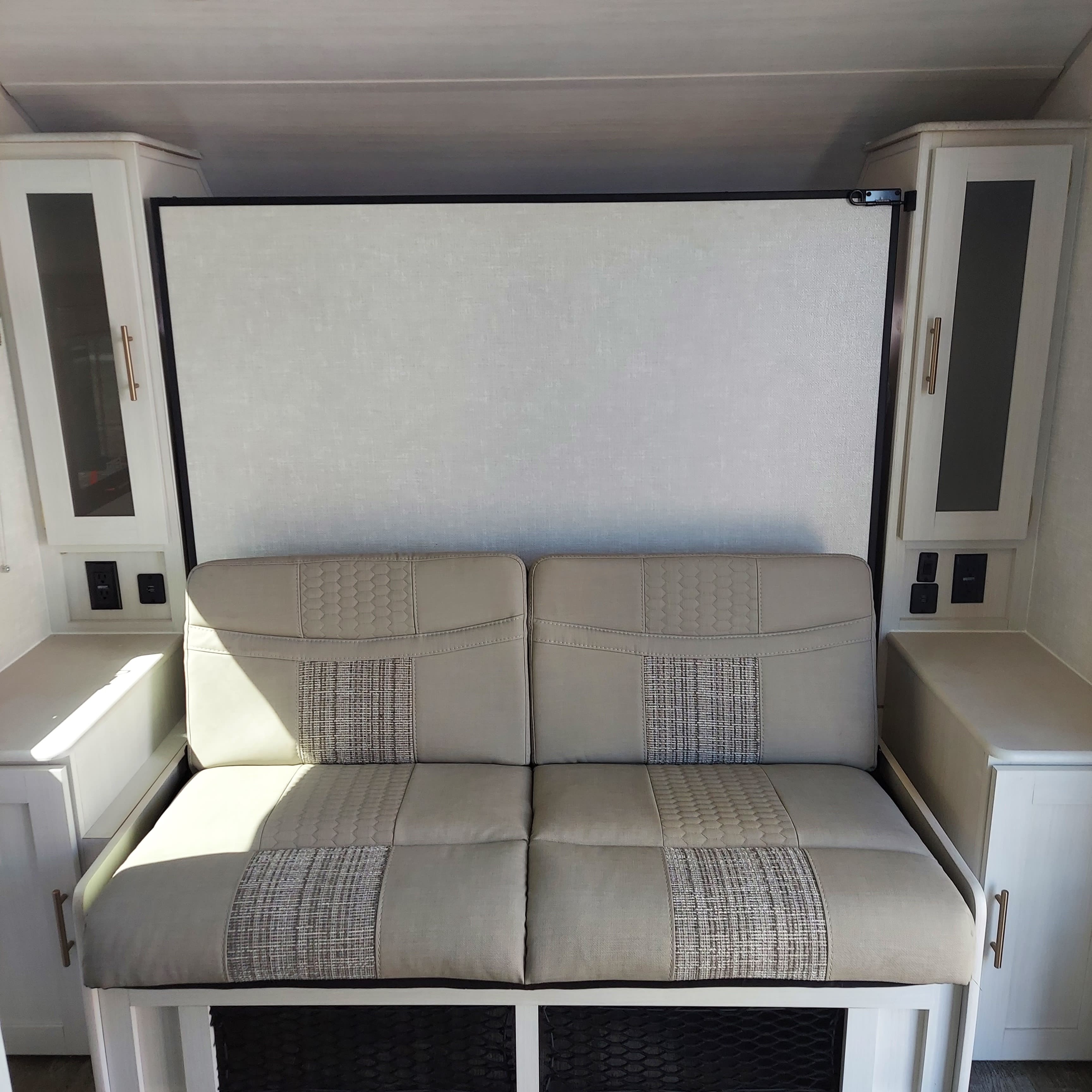 Inside an RV rental: A beige sofa bed flanked by cabinets with power outlets, maximizing space for comfortable travel.. R-Pod R-Pod Trailer 2022