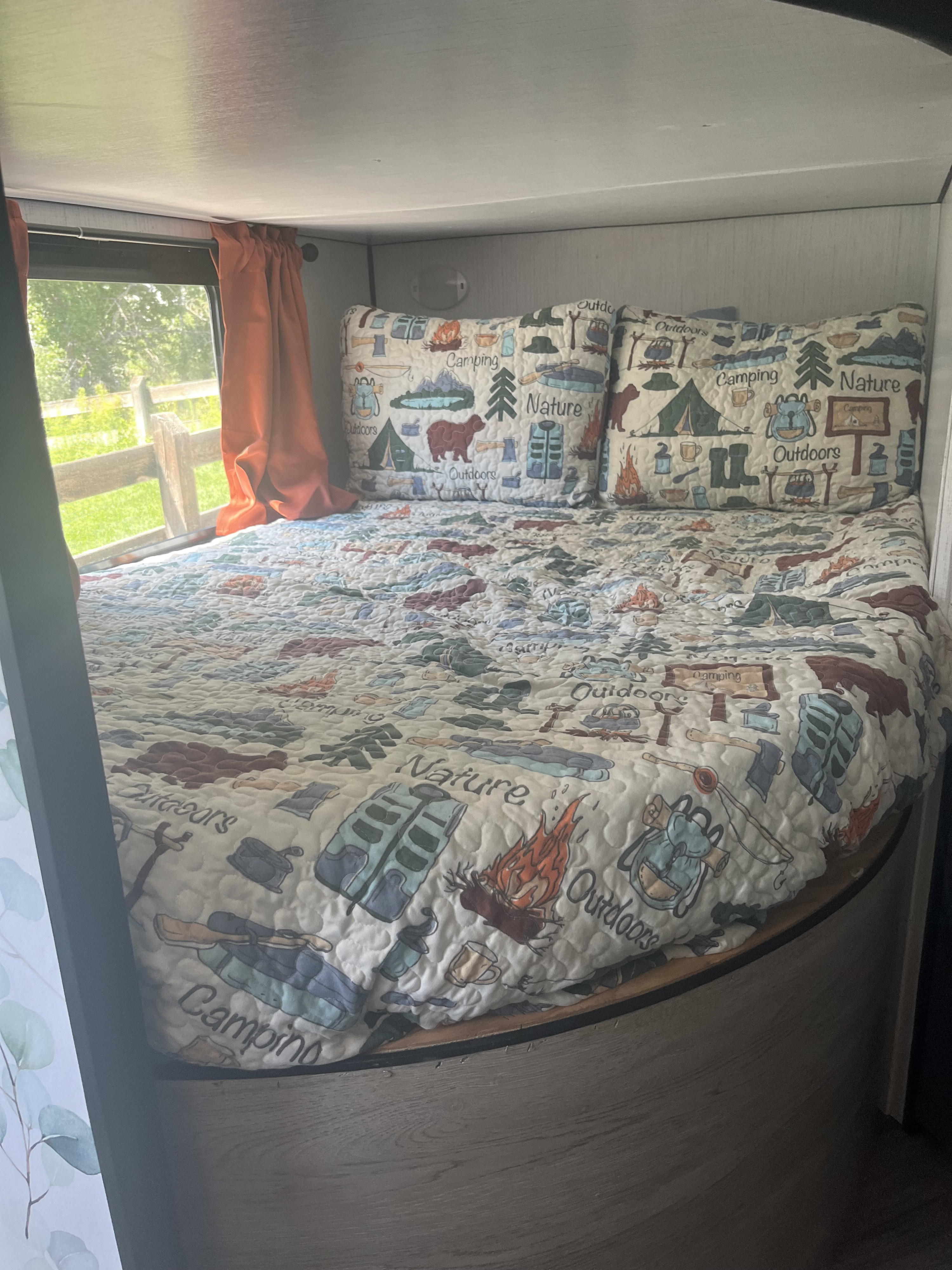 Cozy RV rental bed with a vibrant camping-themed quilt and pillows, ready for your outdoor adventures.. Heartland RVs Prowler 2022