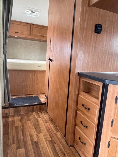 RV rental interior: Wood-look floor leads to a cozy bedroom with bed and cabinets, plus modern kitchen storage and controls.. Thor Majestic 2018
