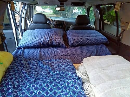 Cozy RV rental interior shows blue patterned bedding and pillows for a comfortable car camping setup in a converted vehicle.. Xplorer Explorer 2007