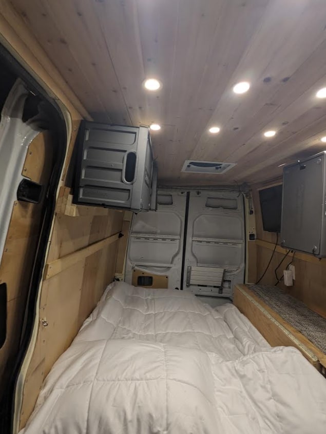 Spacious RV rental interior with a cozy bed, wooden ceiling, and mounted storage. Perfect for mobile living.. Mercedes Benz Sprinter 2500 2014