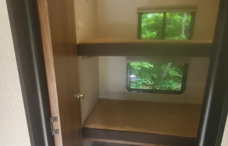 Cozy RV rental bunk beds, each with a window showcasing green nature. Ideal sleeping space for travel trailer adventures.. Forest River Coachmen Chapparal Lite 2019