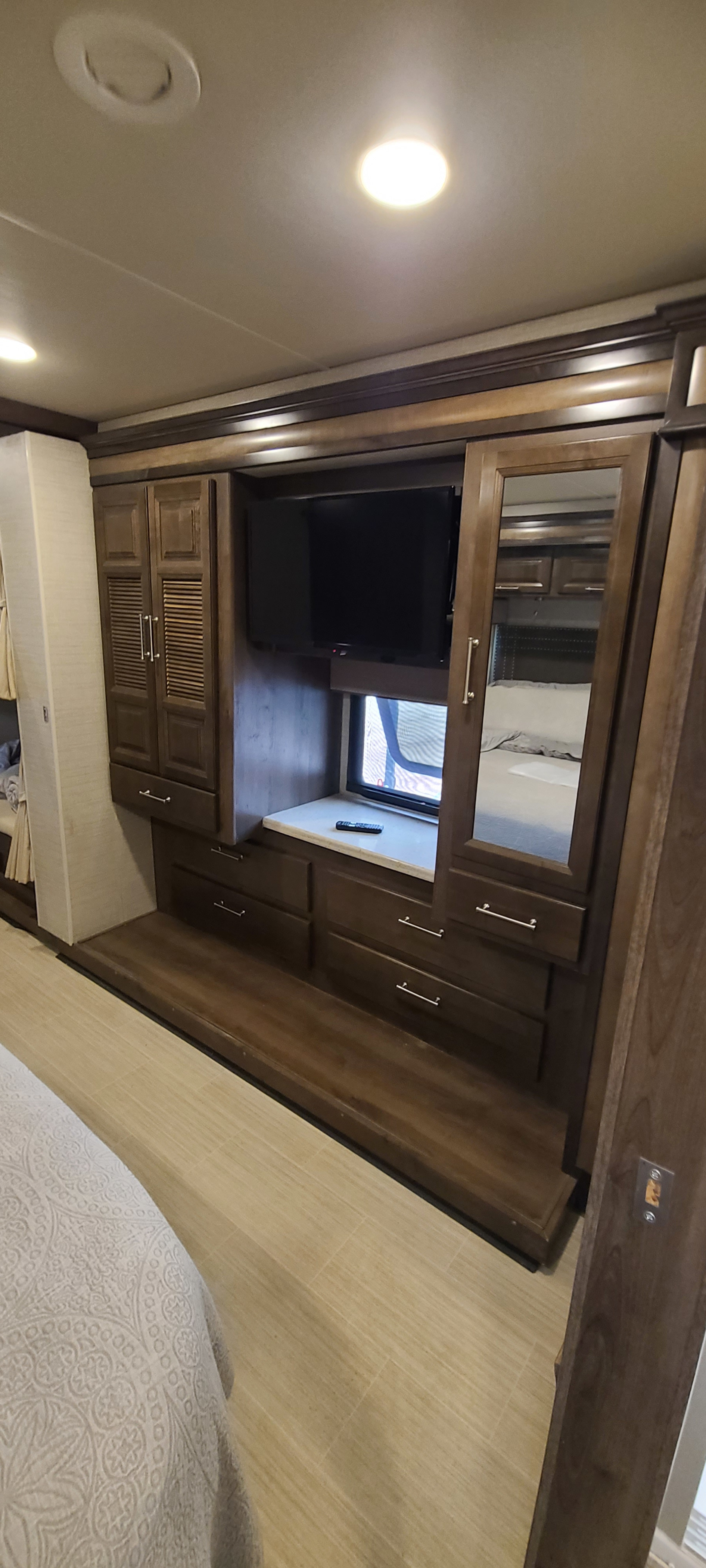 This RV rental bedroom features a mounted TV, storage cabinets, and drawers. A comfortable bed is in the foreground.. Entegra Coach Vision XL 2020