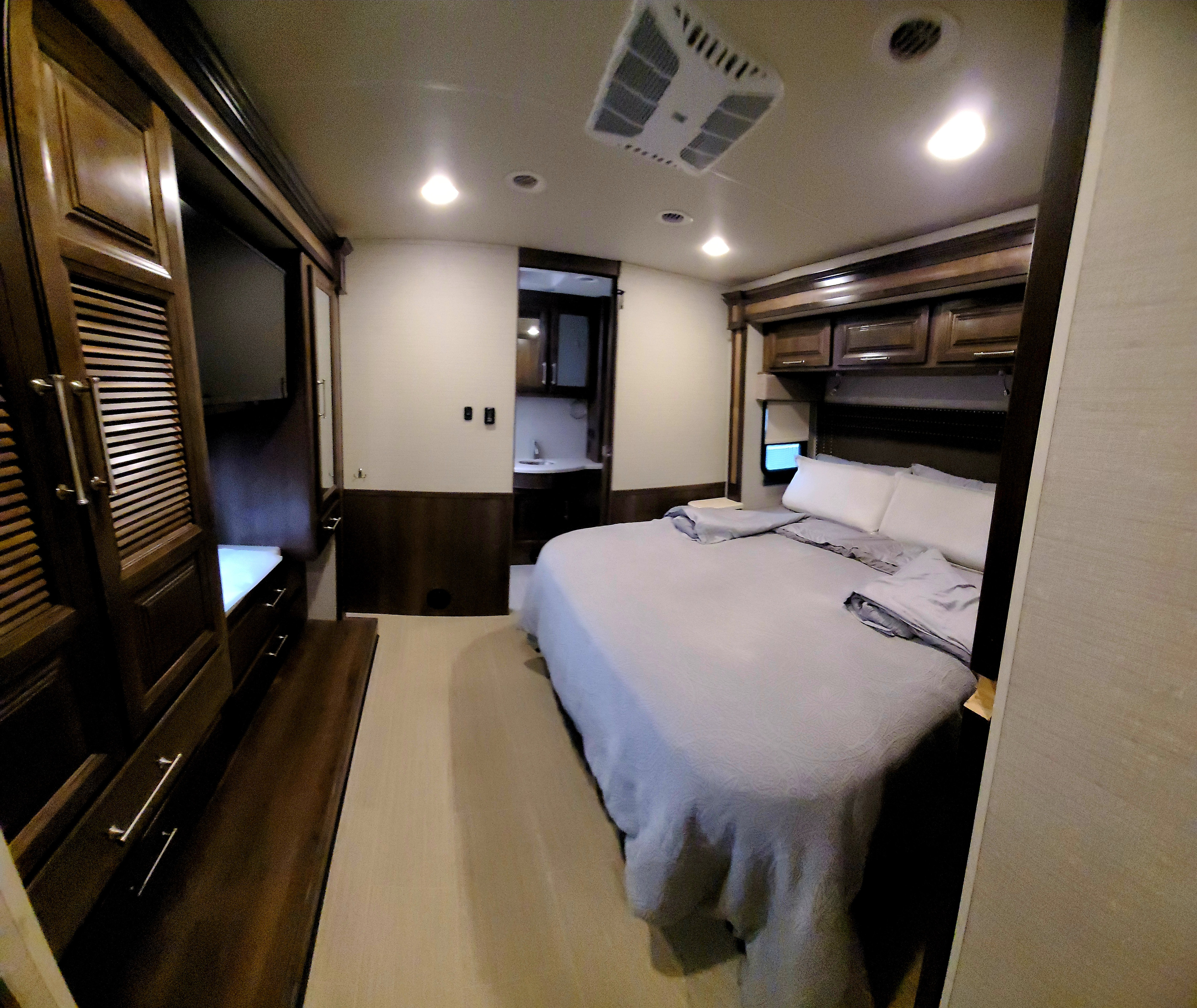 Well-appointed RV rental bedroom. Features a large bed, dark wood cabinetry, and an ensuite bath area.. Entegra Coach Vision XL 2020