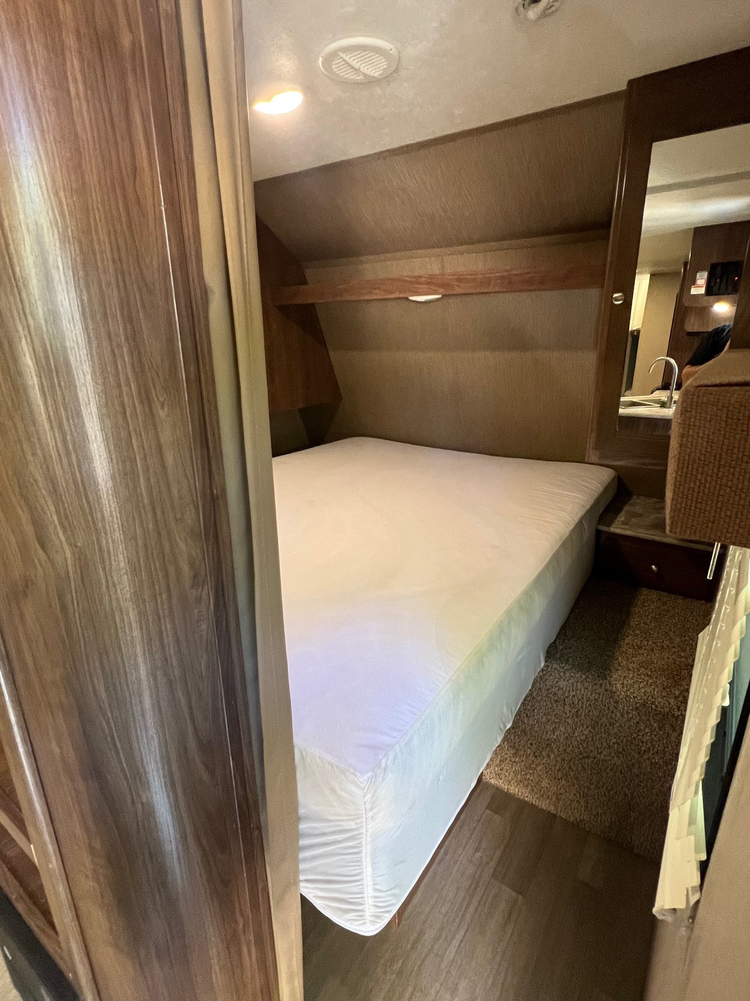 Inside an RV rental: a cozy bedroom features a bed, overhead shelf, and adjacent bathroom vanity.. Dutchmen Lantern 2018