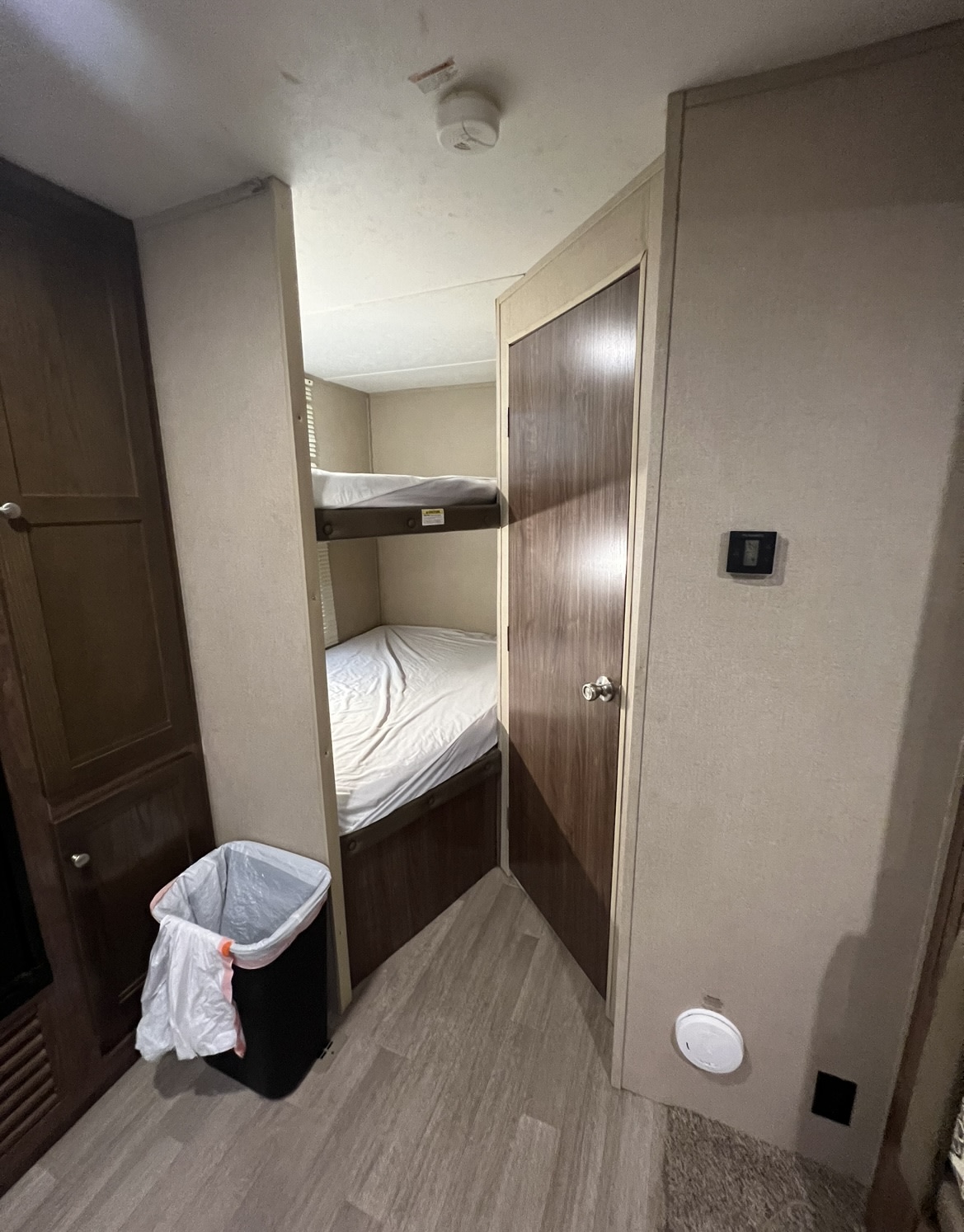 Compact RV rental interior featuring bunk beds, a door, and a trash can, ideal for family travel.. Dutchmen Lantern 2018