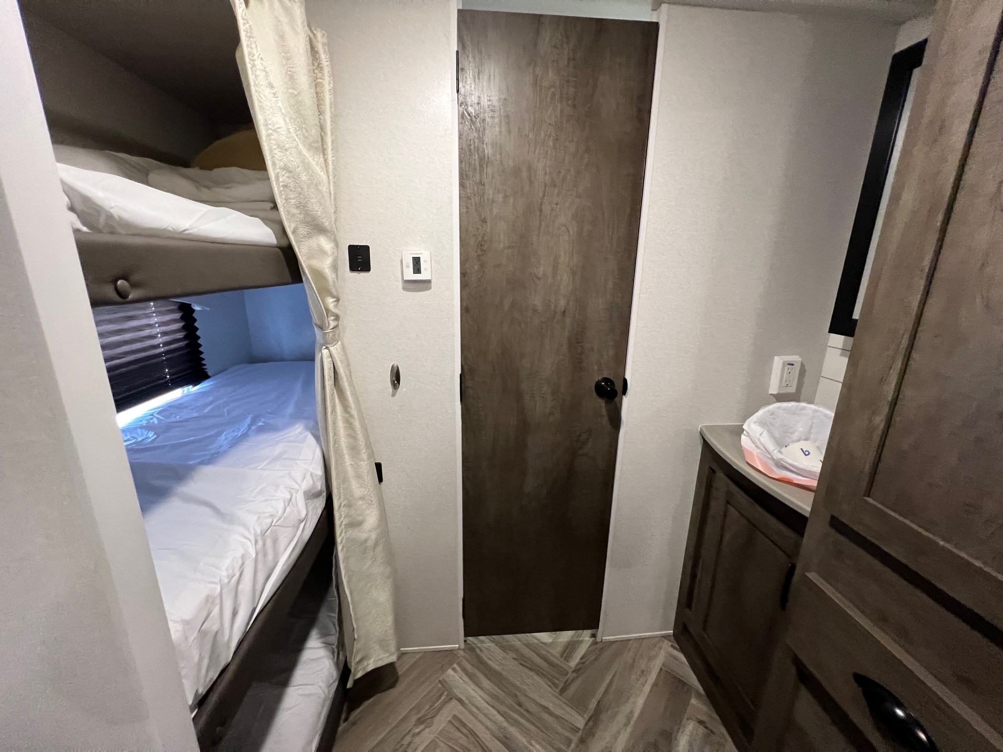 RV rental interior view: bunk beds with white linens, a wooden door, and a small vanity area.. Forest River Evo 2020