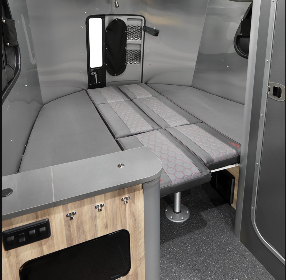 Compact RV rental: versatile interior with a full-size convertible bed, patterned cushions, and a small built-in counter.. Airstream Basecamp 2022