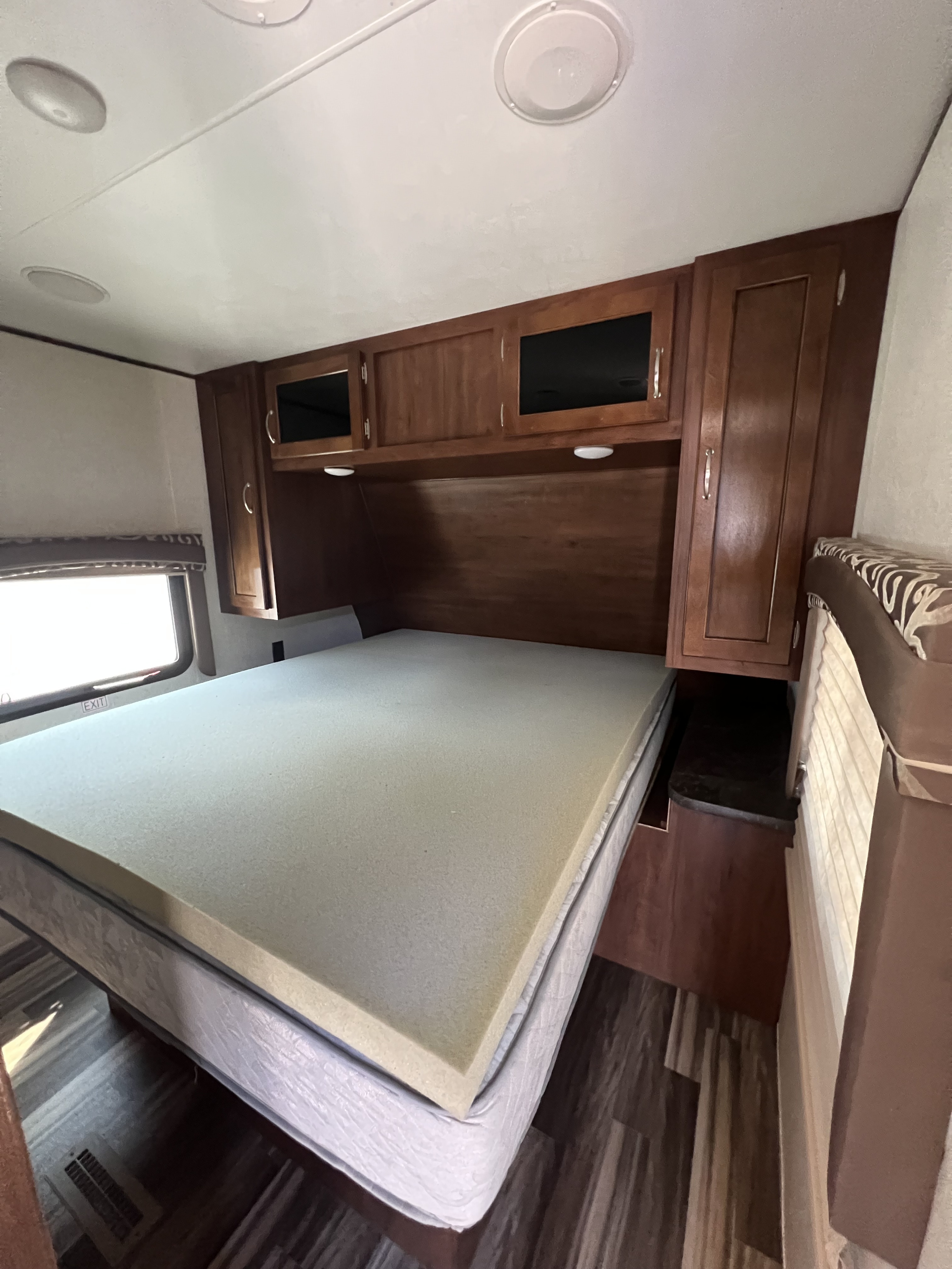 Inside an RV rental: a cozy bedroom with a bed, foam topper, overhead wood cabinets, and window.. Jayco Jay Flight 2017
