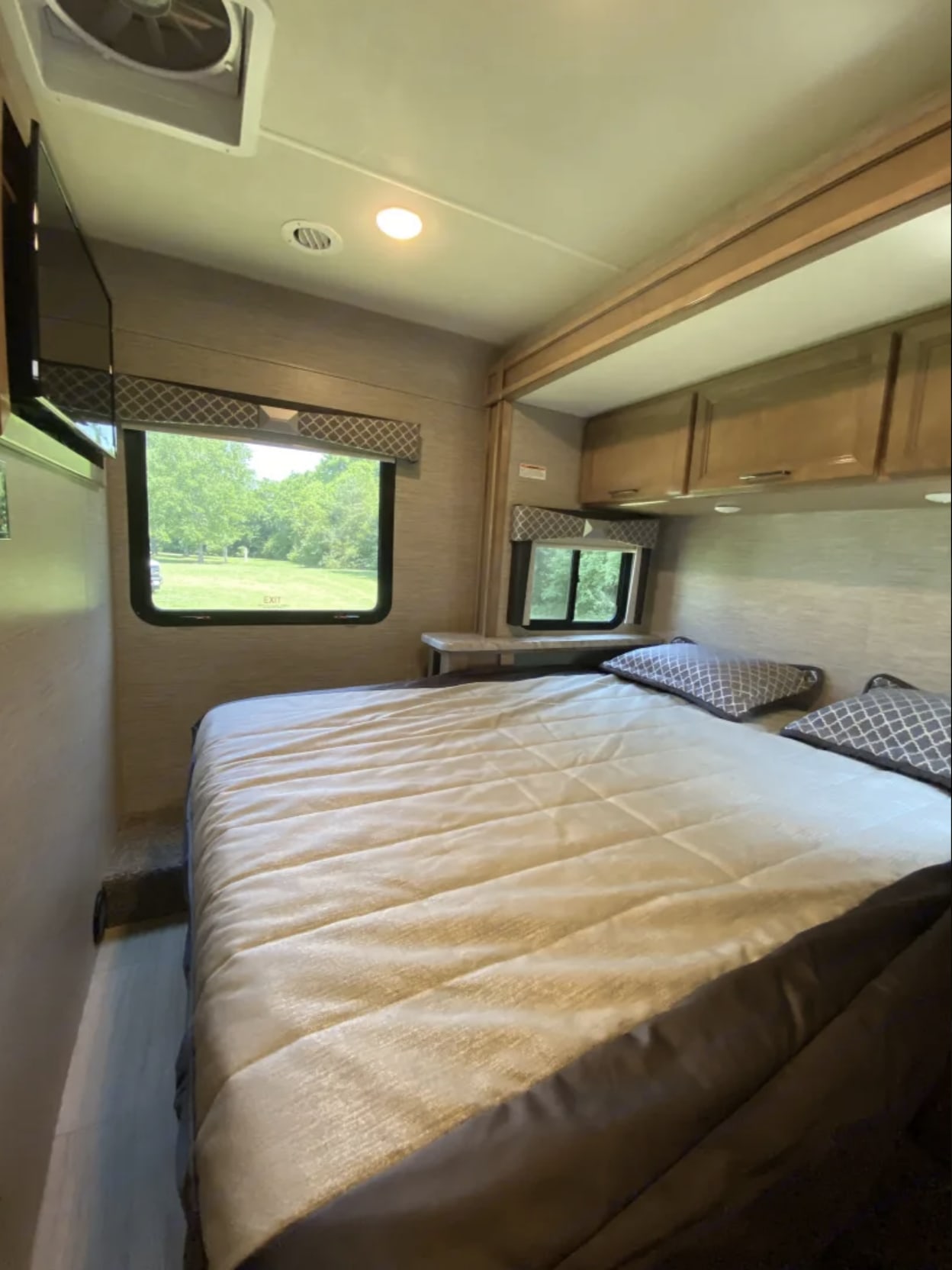 Spacious RV rental bedroom with a comfortable bed, windows, overhead cabinets, and a mounted TV for your travel comfort.. Thor Quantum 2021