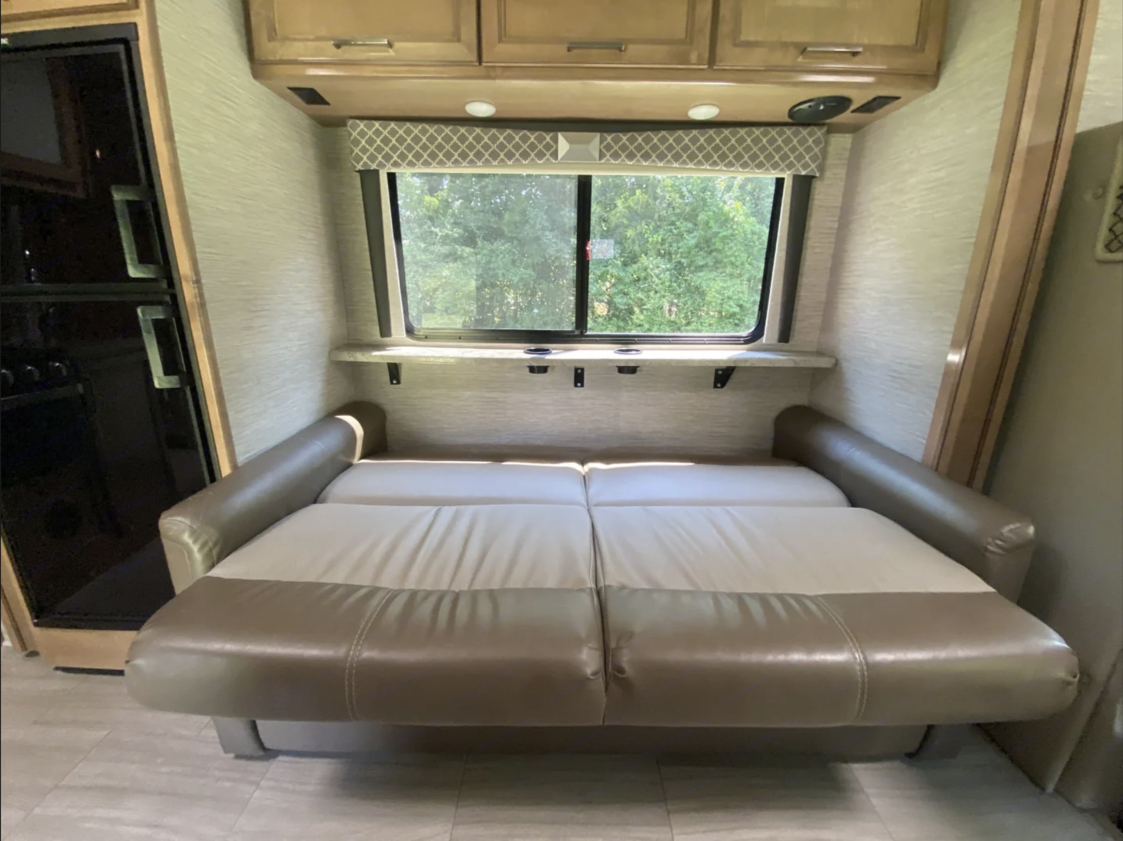 RV rental's versatile living area: a two-tone sofa converts to a bed, with a window view & overhead cabinets.. Thor Quantum 2021
