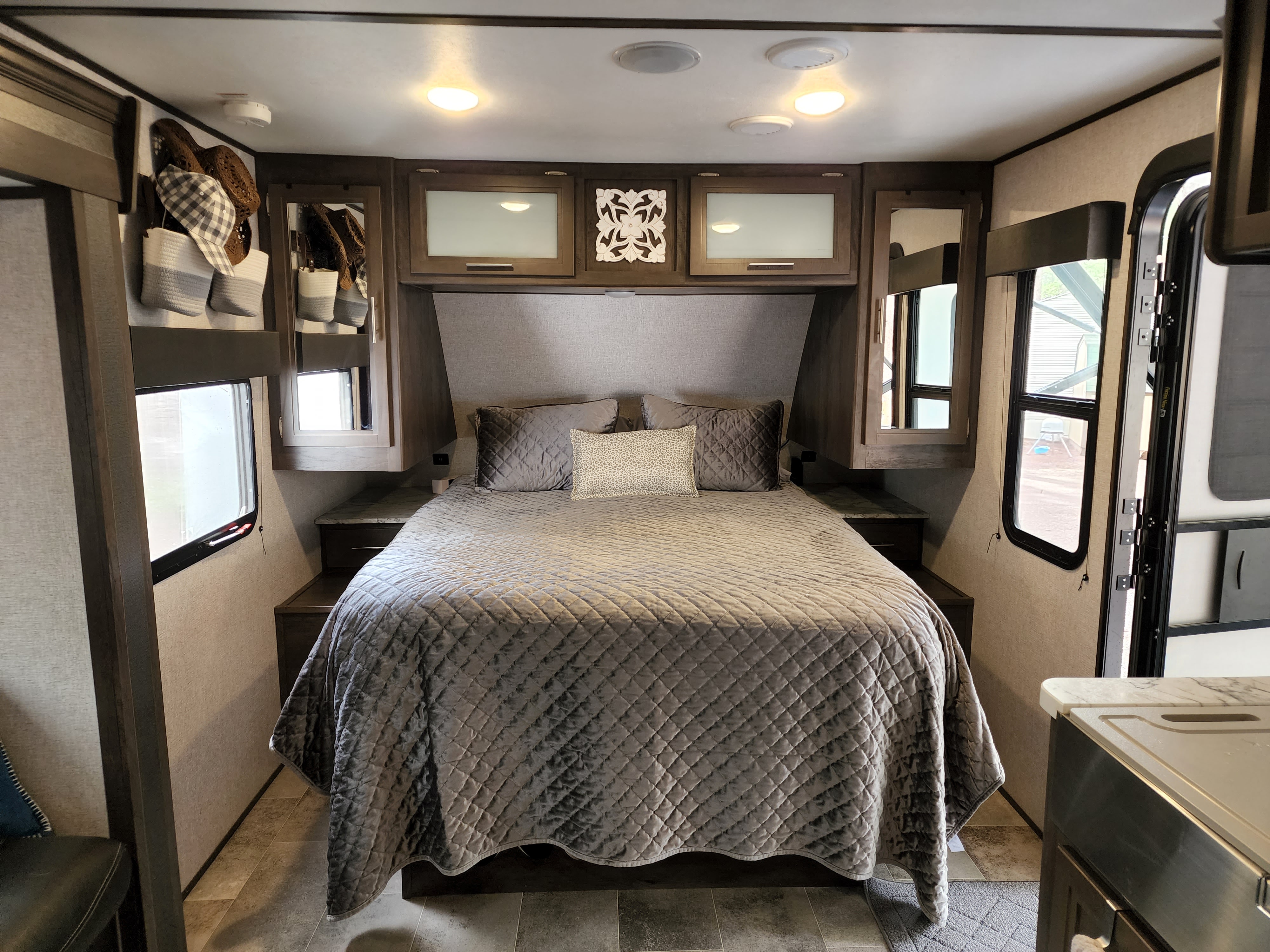 Inside an RV rental: a spacious, cozy bedroom with a quilted bed, overhead cabinets, and large windows.. Dutchmen Coleman Light 2020