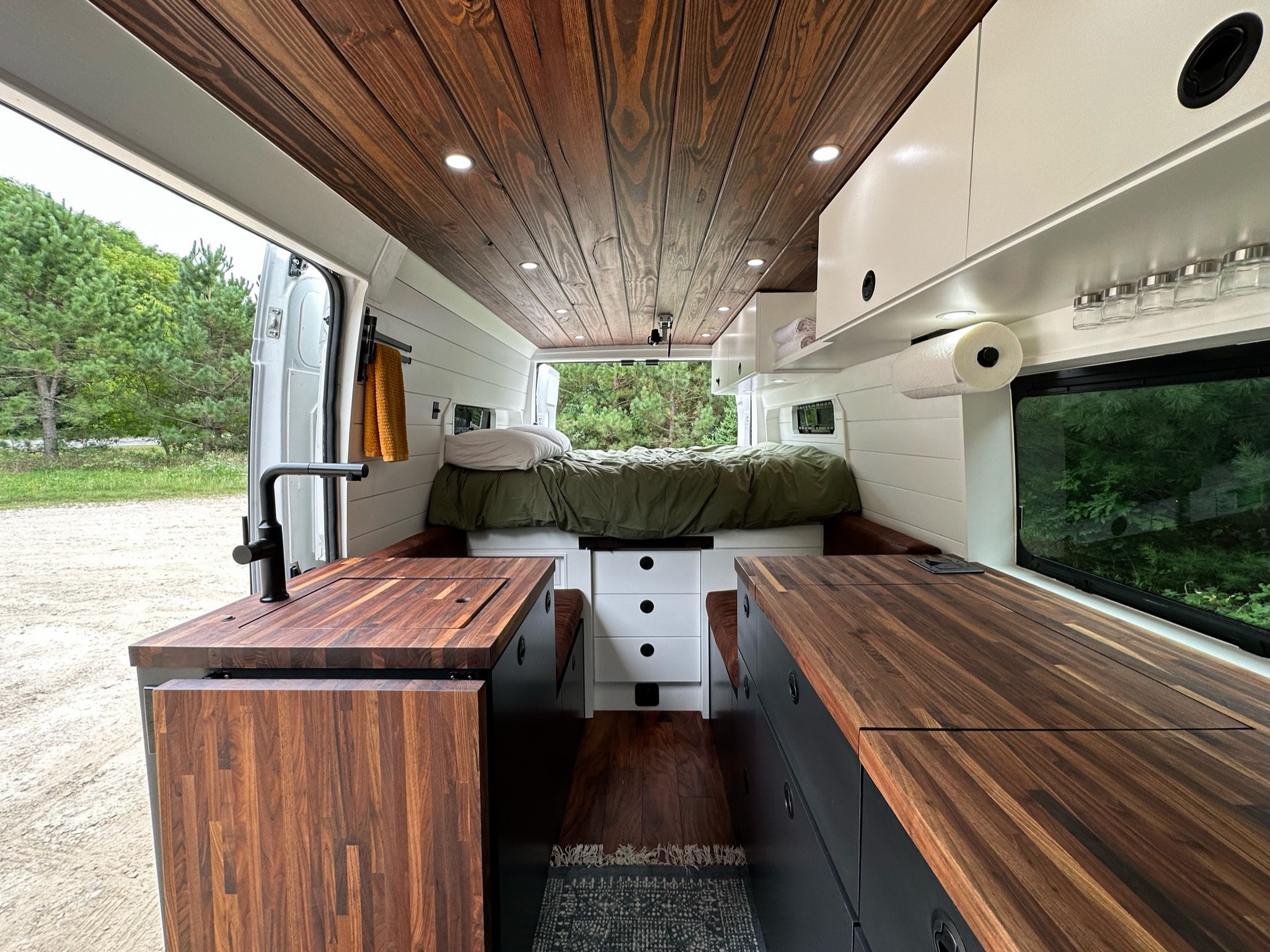 Bright RV rental interior features dark wood ceiling & counters, modern kitchen, & cozy rear bed.. RAM ProMaster 2500 2022