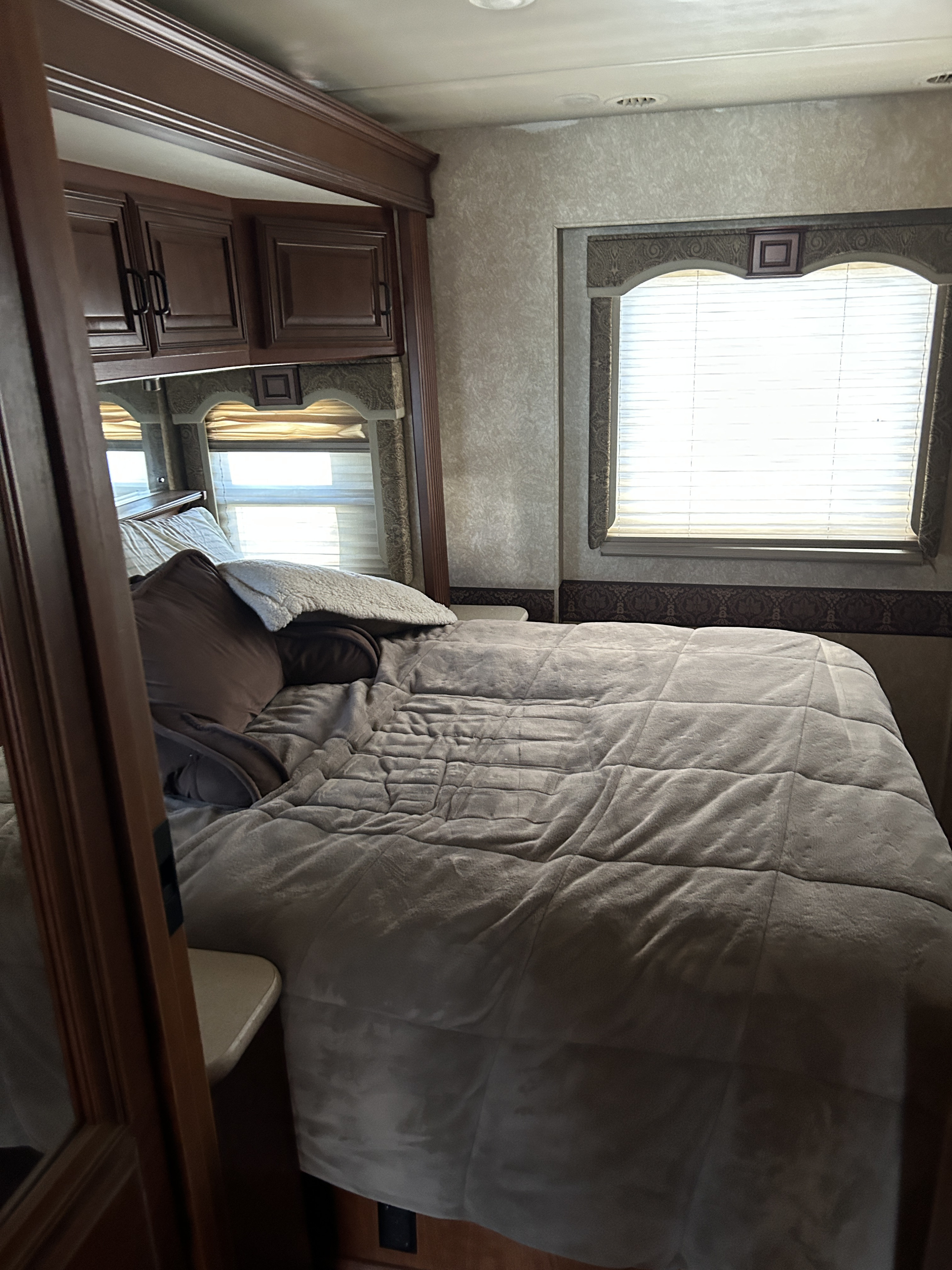 Cozy RV rental bedroom with a comfy bed, overhead cabinets, and bright windows, perfect for relaxation on the road.. Four Winds Windsport 2010