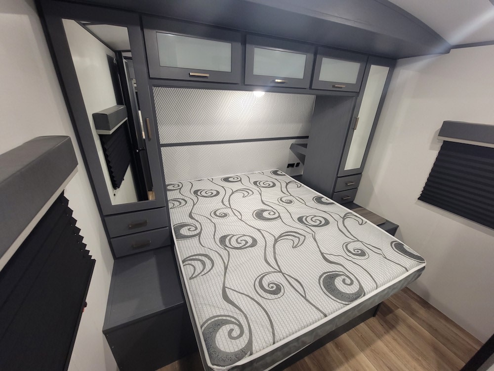 RV rental bedroom featuring a comfortable bed with grey patterns, built-in dark grey cabinetry, and a mirrored wardrobe.. Keystone RV Bullet Ultra Lite 2023