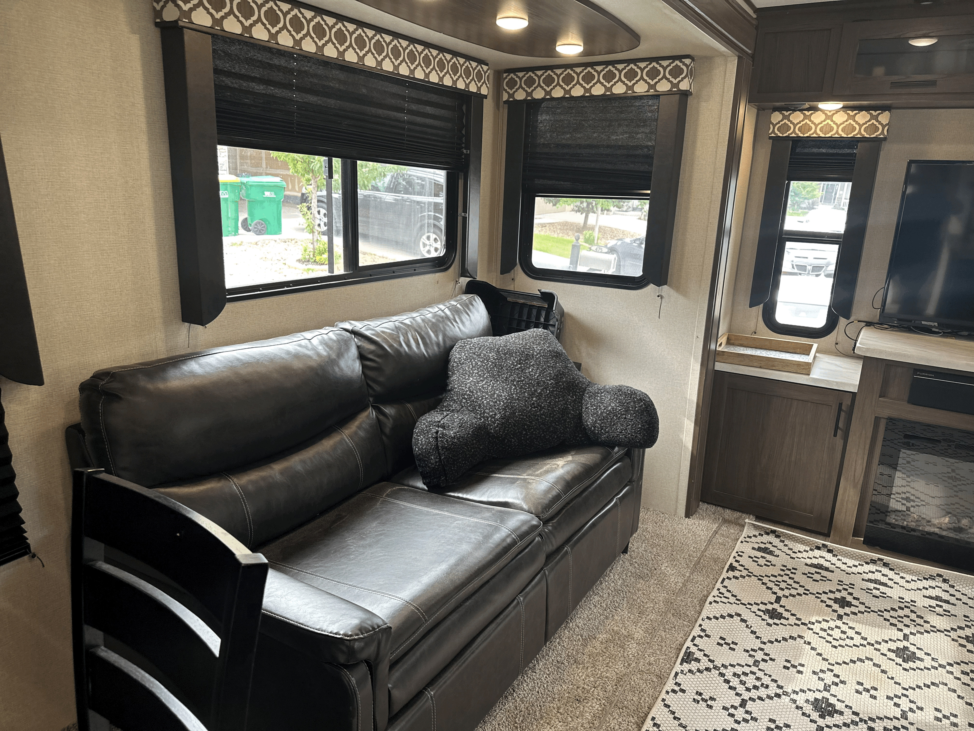 Comfortable RV rental living space featuring a dark leather sofa, windows with patterned valances, and a cozy rug.. Forest River Lacrosse Luxury Lite 2020