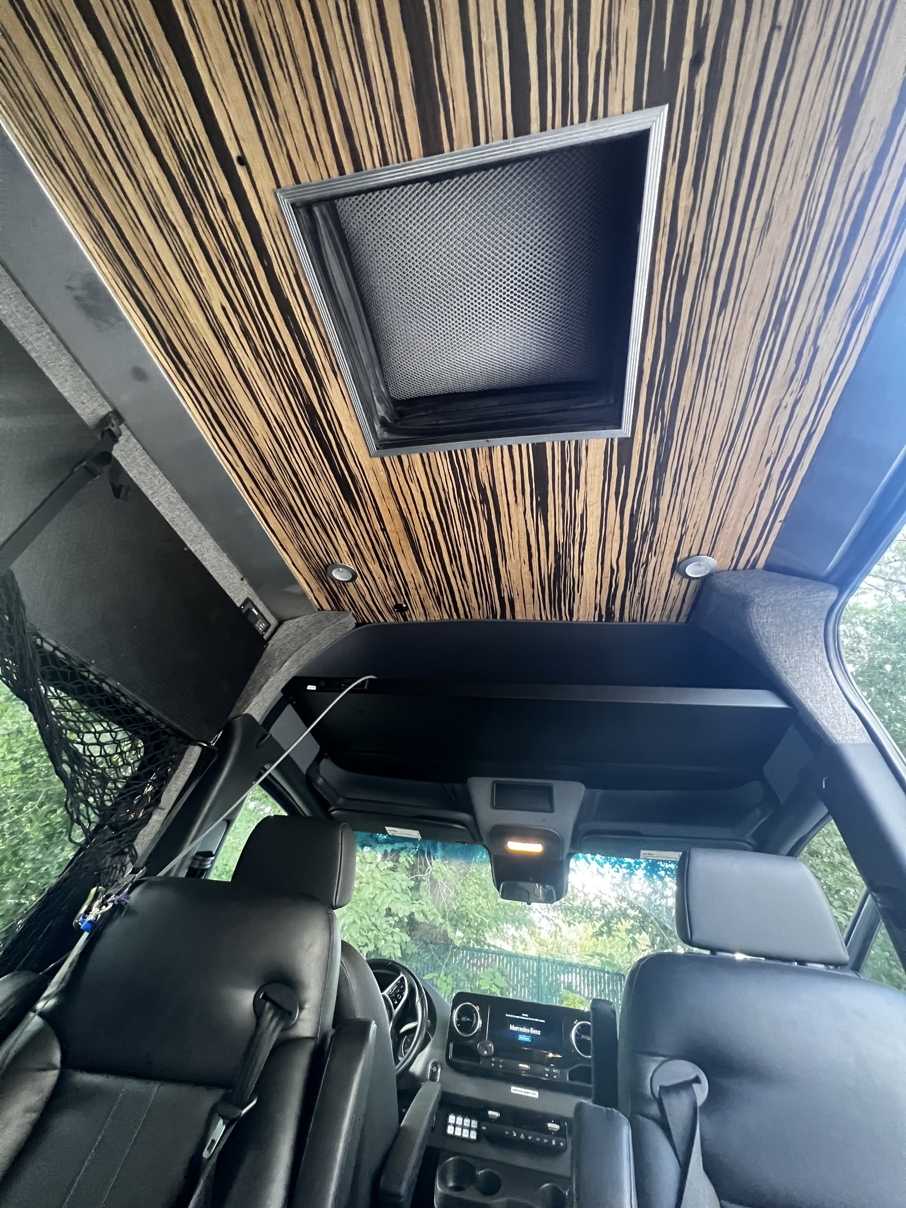 Inside a modern rv rental: unique striped wood ceiling, overhead vent, comfy black seats, and controls. Perfect road trip comfort.. Mercedes-Benz Sprinter 2019