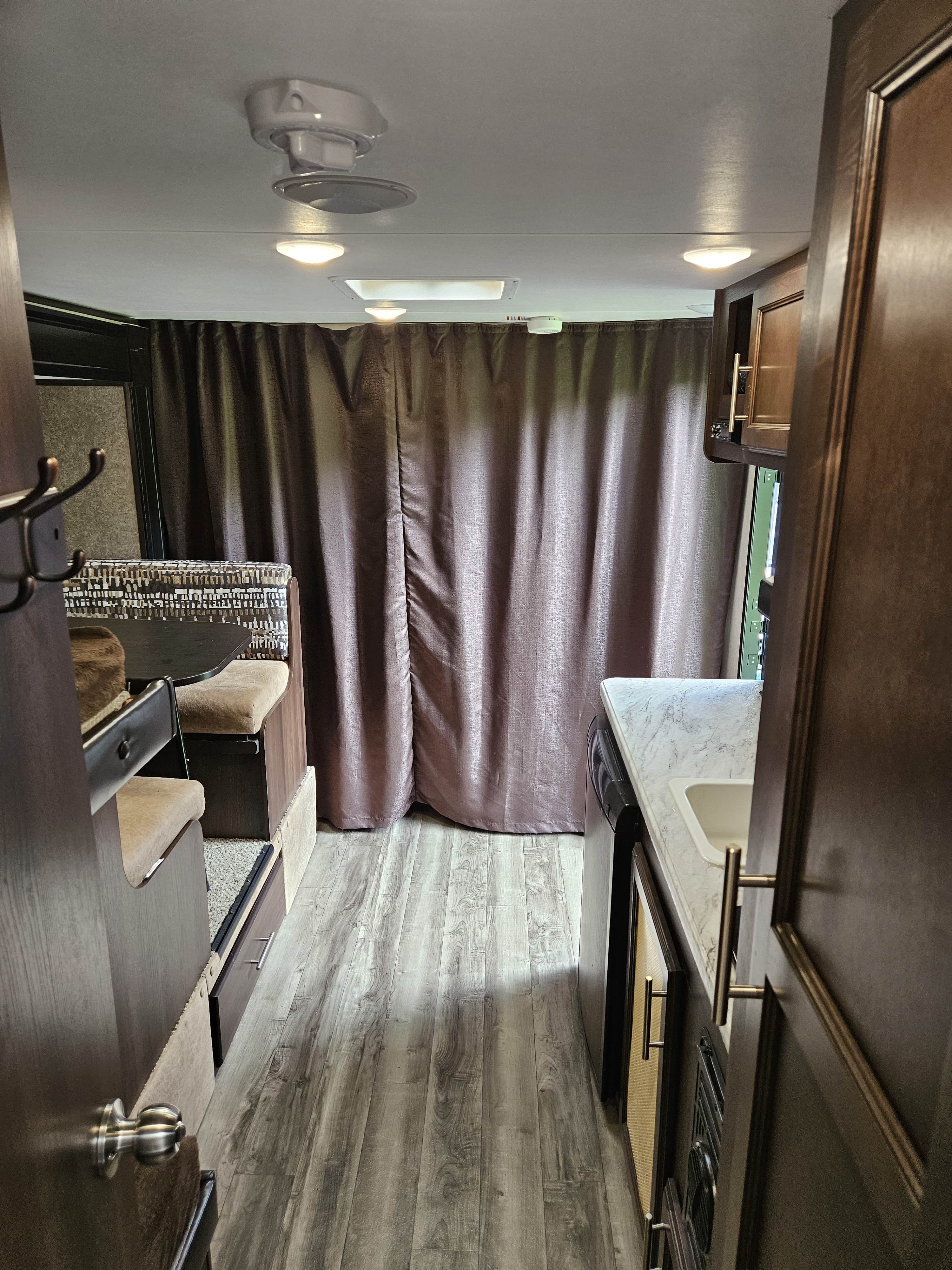 RV rental interior. Aisle view of compact kitchen with sink, dinette with patterned cushions, bunk beds, and wood-look floor.. Jayco Jay Flight SLX 2019