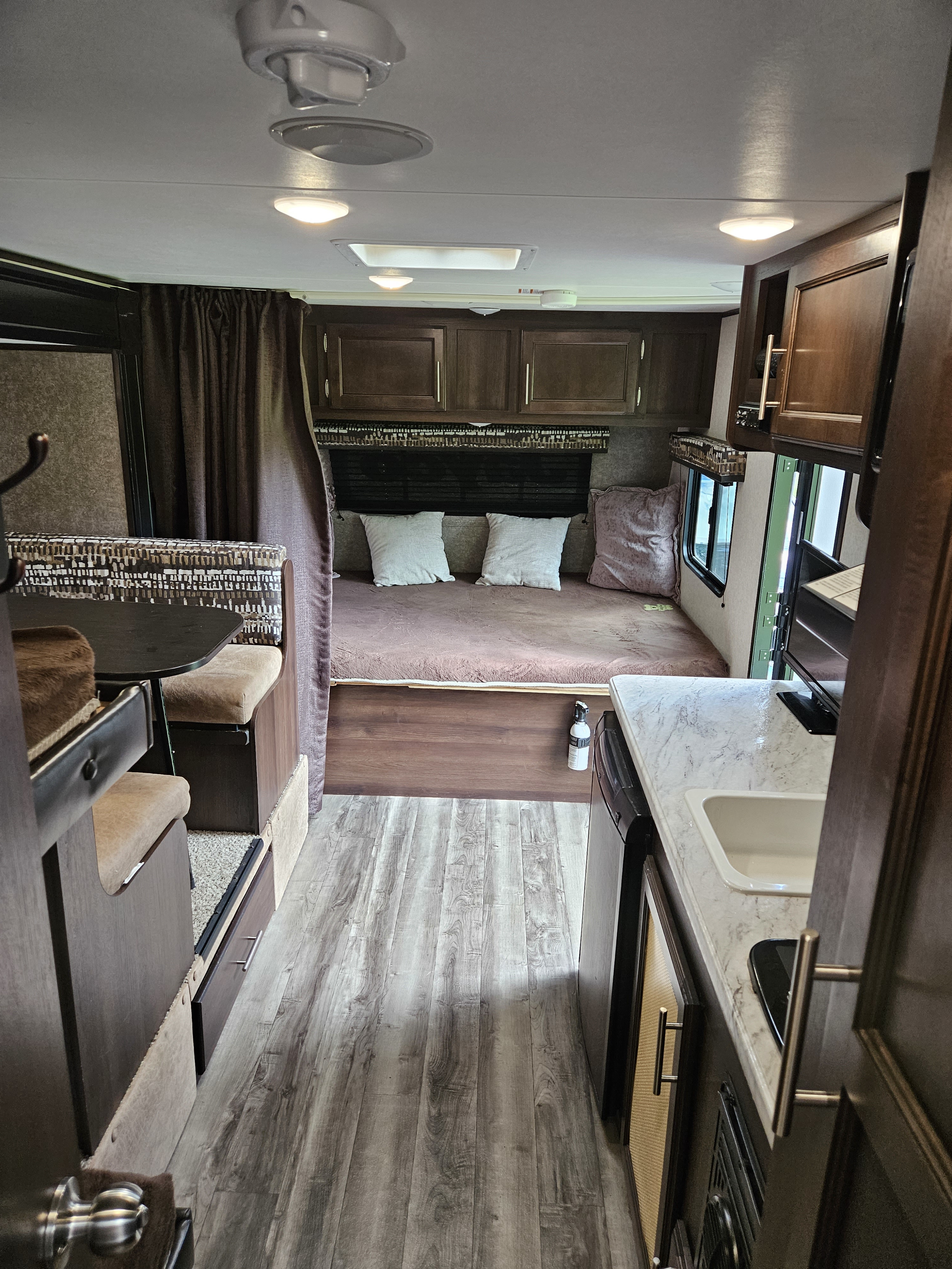 Inside a modern RV rental: a compact living space with a bed, dinette, and kitchen area, featuring wood-look flooring.. Jayco Jay Flight SLX 2019