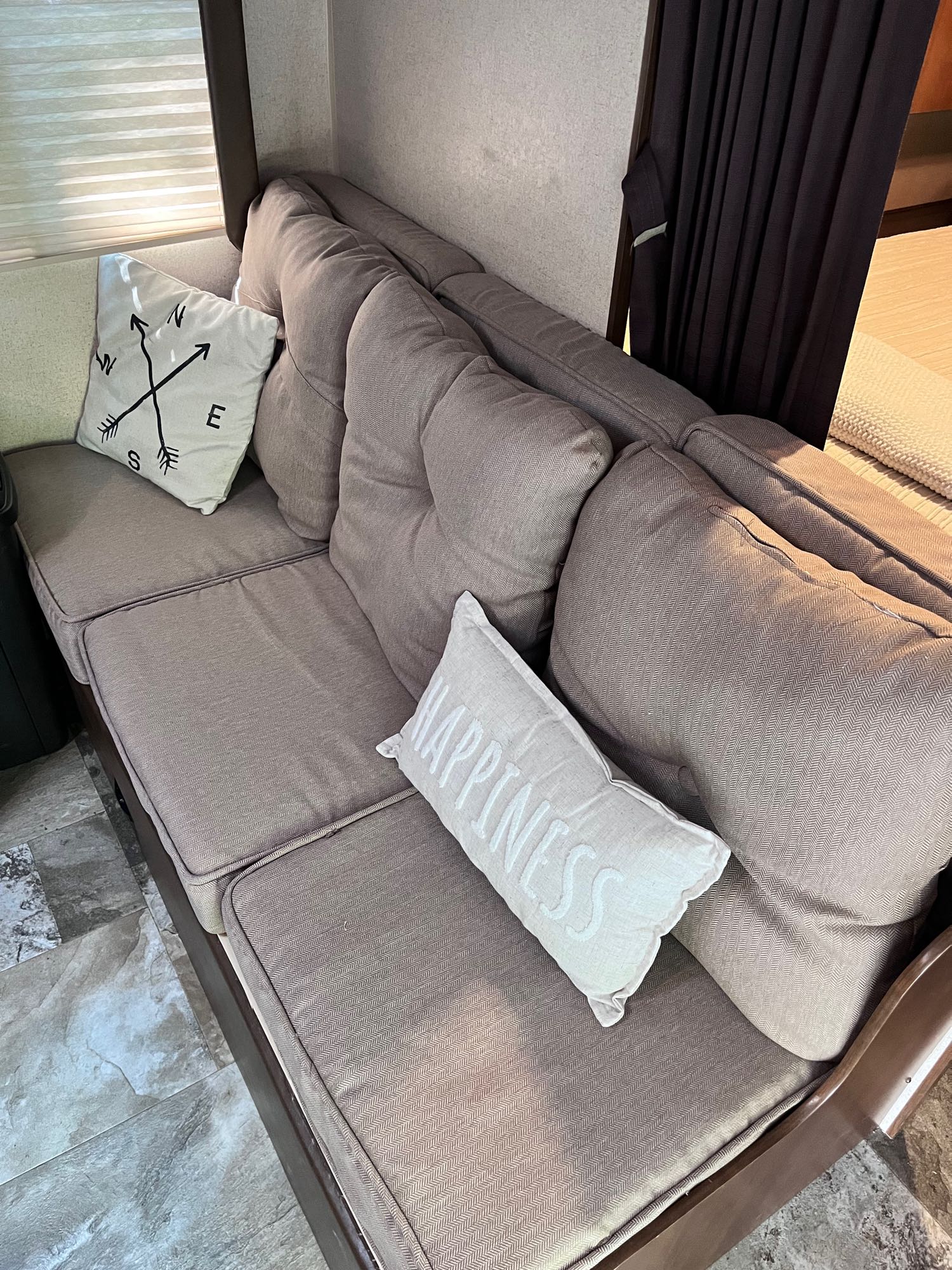 Cozy RV rental interior with a comfy sofa, compass, and 'Happiness' pillows, perfect for relaxation on the go.. Jayco Jay Flight 2015