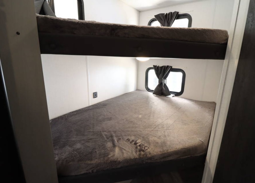 This RV rental interior features comfortable bunk beds with windows, providing a cozy sleeping area in a camper.. Forest River Wildwood FSX Plantium 2022