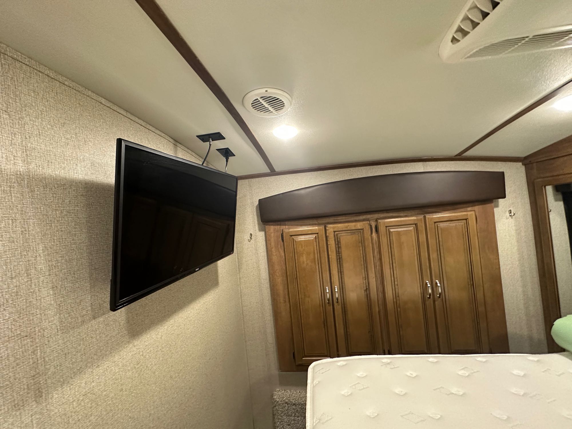 RV rental bedroom showcasing a wall-mounted TV, wood cabinets, and a comfortable bed. Ideal for travel.. Keystone RV Laredo 2018
