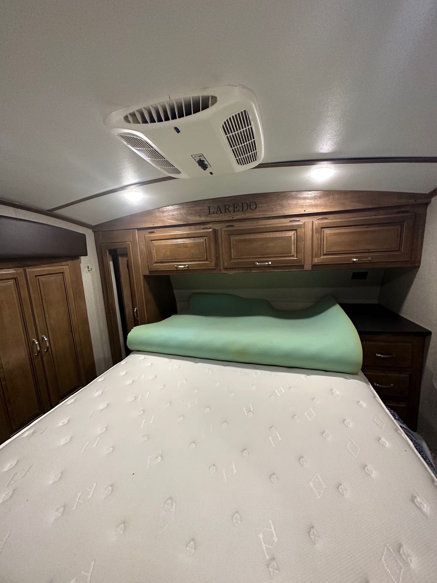 RV rental bedroom with a large mattress, green foam topper, wood cabinets, and ceiling AC unit.. Keystone RV Laredo 2018