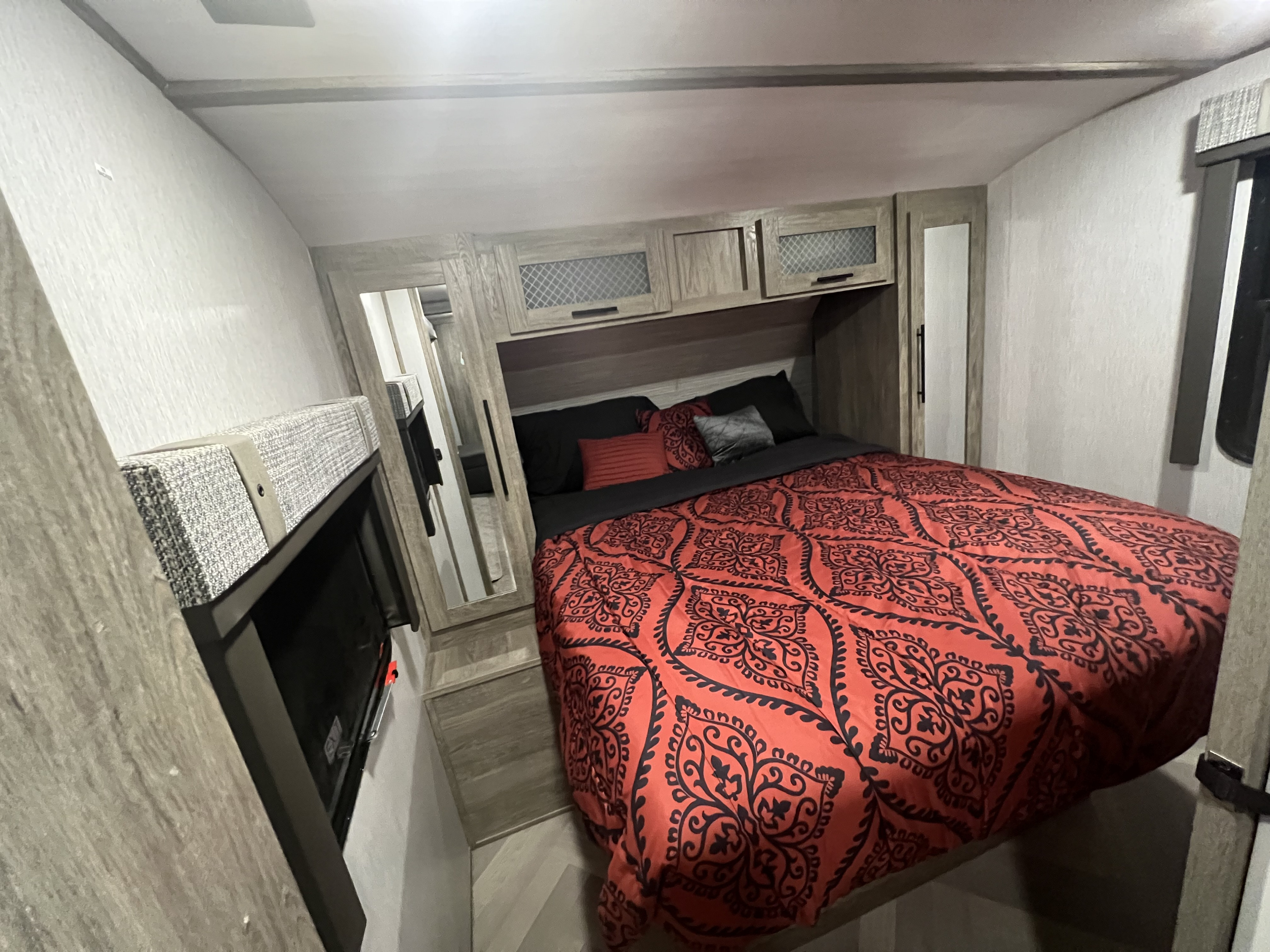 Experience comfort in this RV rental's spacious bedroom, featuring a vibrant bed, overhead storage, and a mounted TV.. Heritage 22RBHL 2022