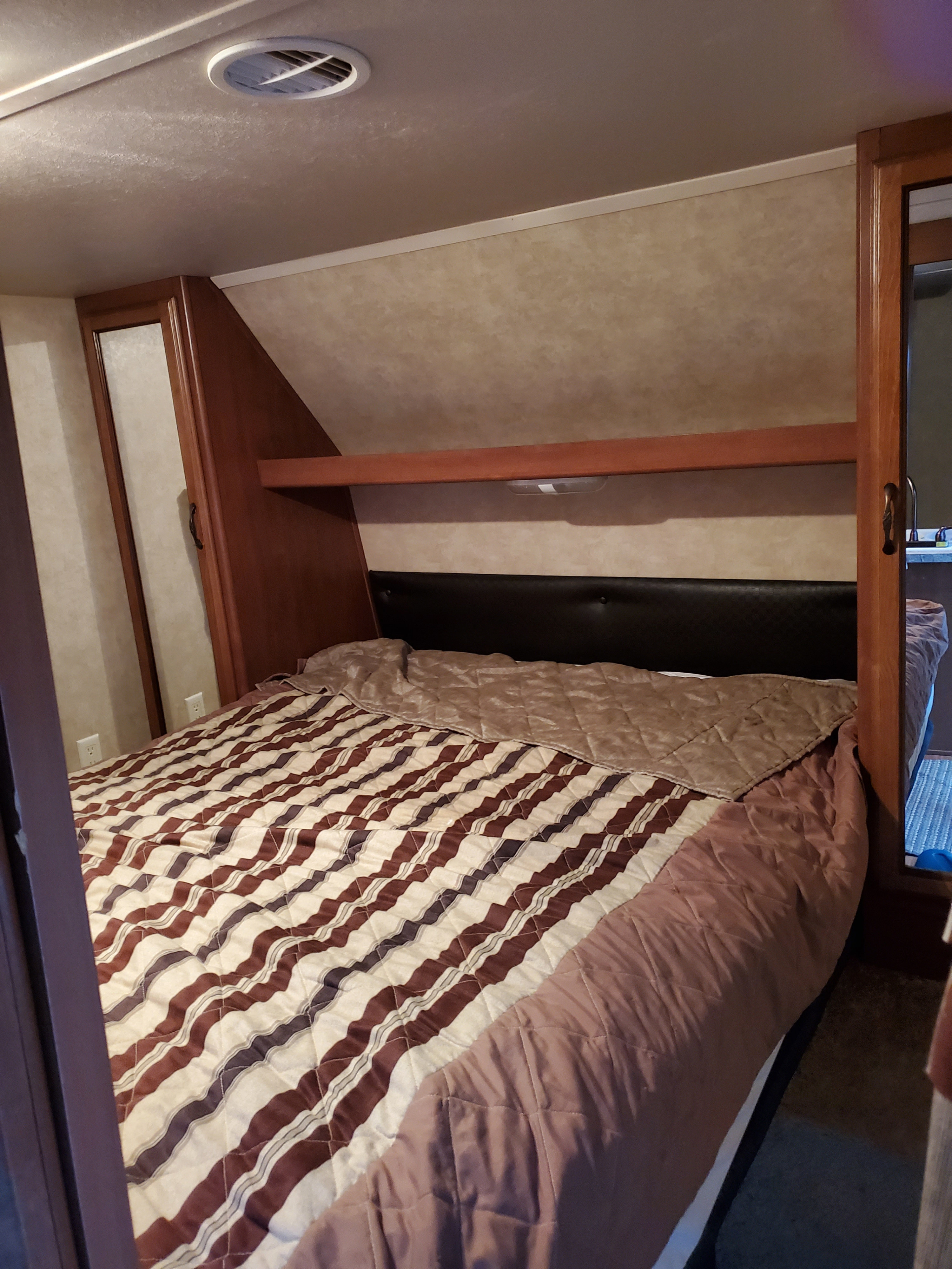 Cozy RV rental bedroom with a striped bed, black headboard, wooden cabinetry, and ceiling vent. Compact space.. Forest River Salem 2014