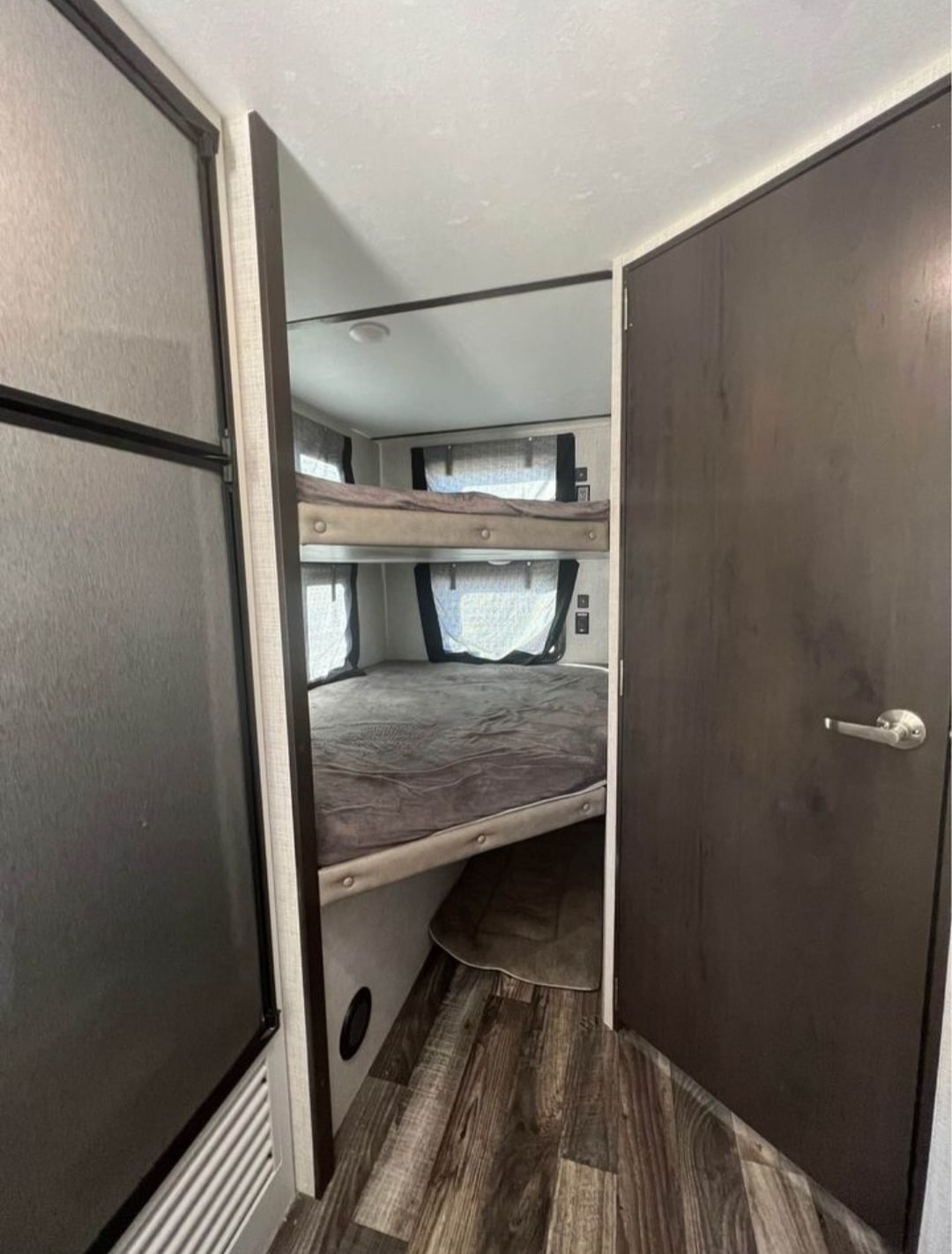 Cozy RV rental interior: view of bunk beds (two high) with mattresses, alongside a door and refrigerator. Compact sleeping space.. Keystone RV Bullet Ultra Lite 2020
