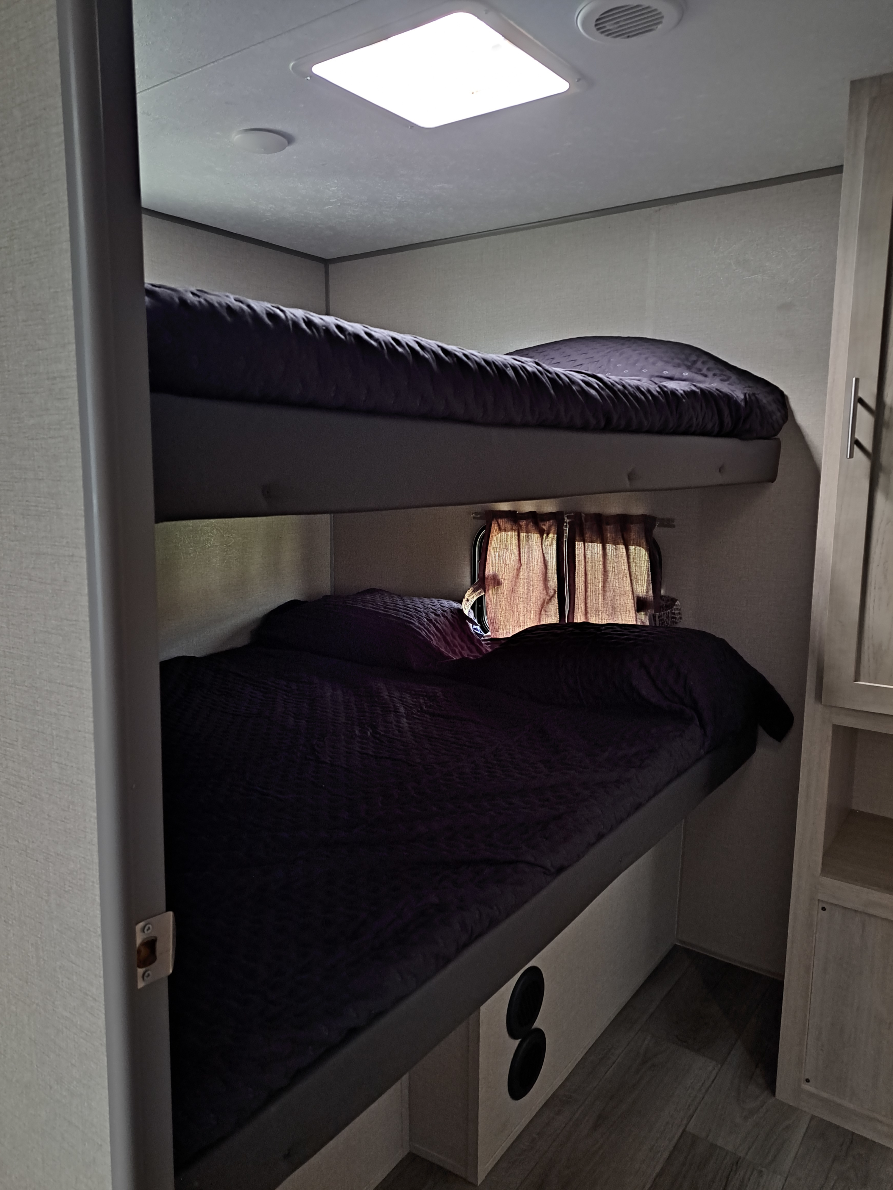 RV rental: Cozy bunk beds with dark bedding, a window with curtains, and integrated speakers in this compact space.. Coachmen Catalina 2023