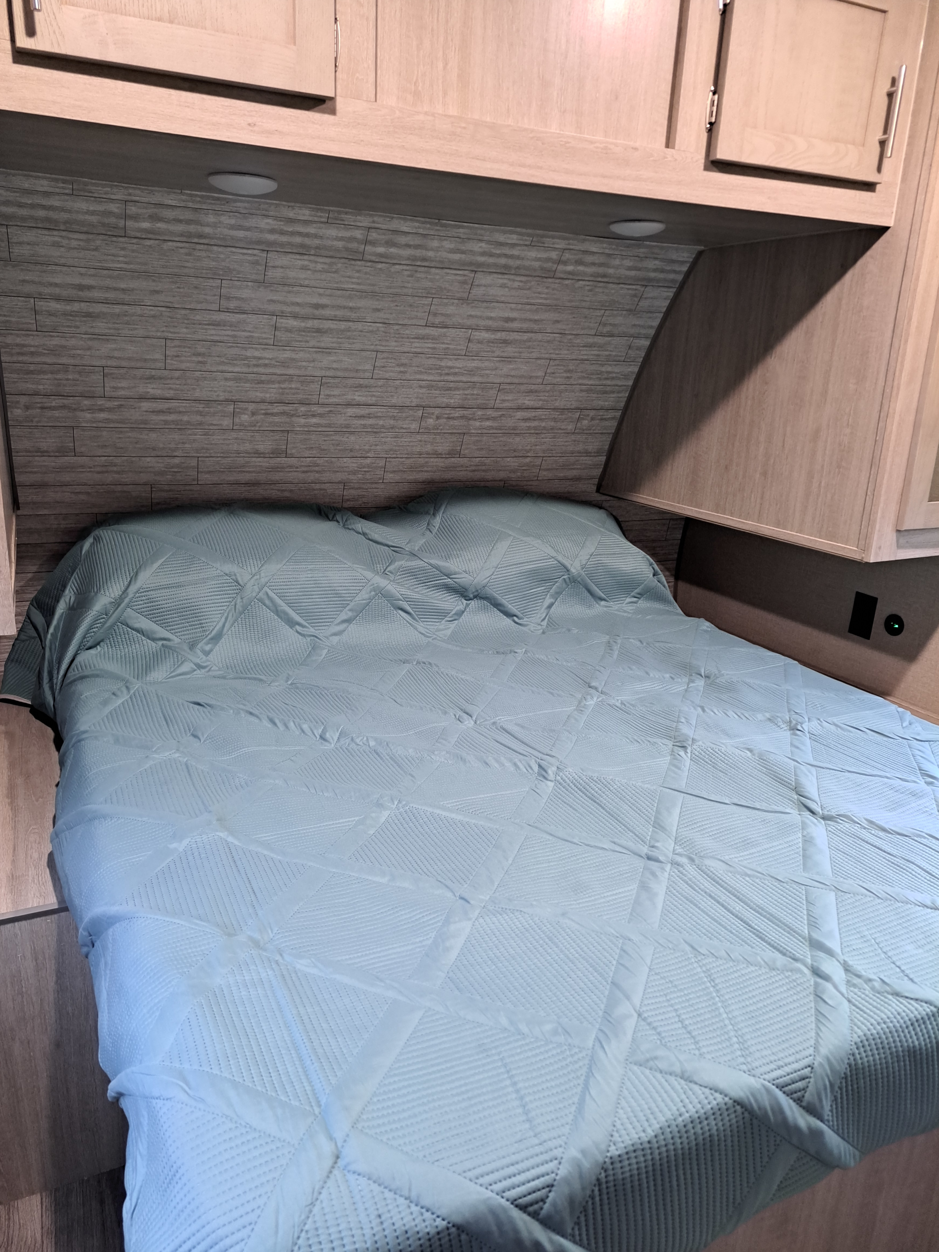 Step into comfort in this RV rental bedroom. Features a light blue quilted bed, wood paneling, and practical overhead cabinets.. Coachmen Catalina 2023